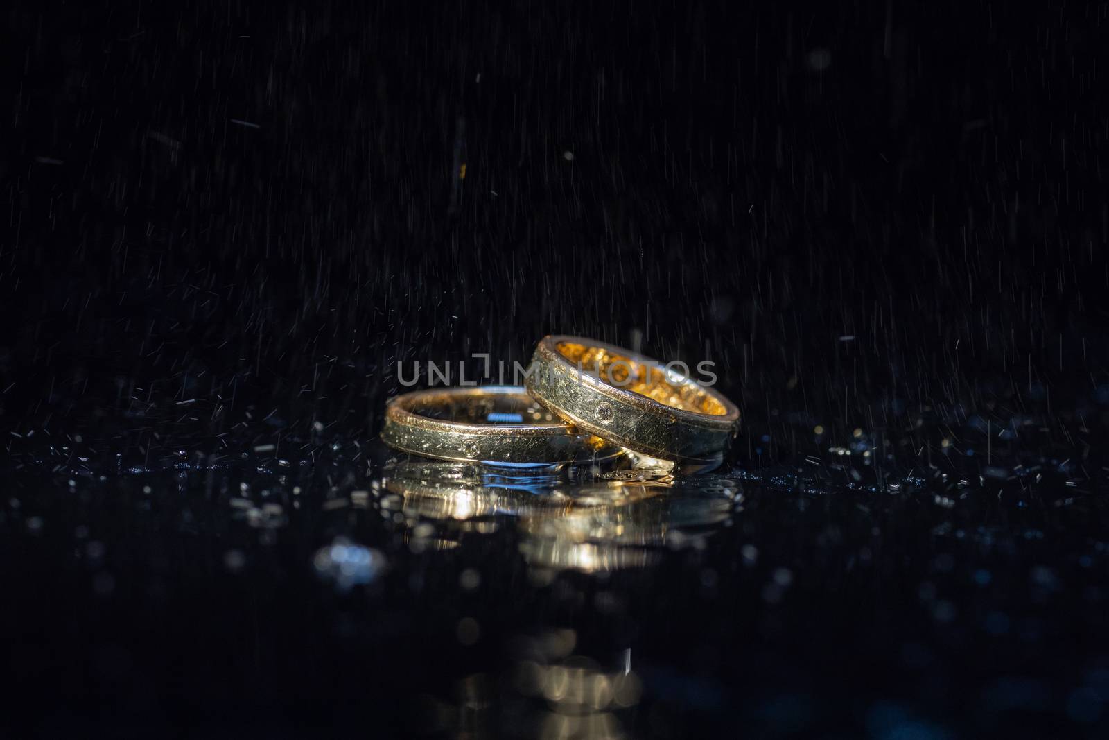 Wedding rings lying on dark surface shining with light close up macro. Water splashes