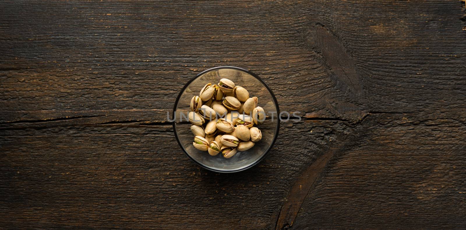 Pistachios in a small plate on a vintage wooden table. Pistachio is a healthy vegetarian protein nutritious food. Natural nuts snacks. by vovsht