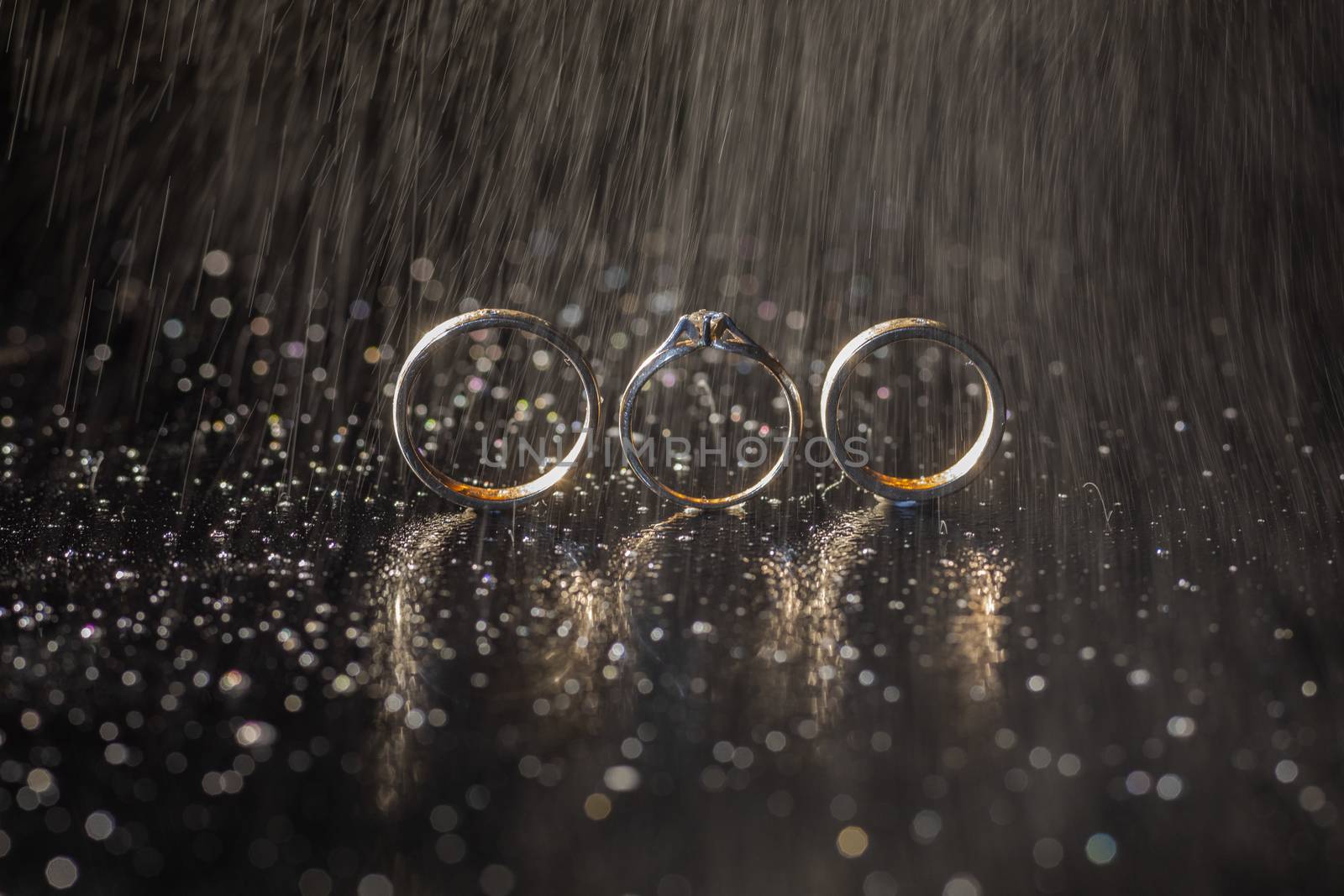 Wedding and engagement rings lying on dark surface shining with light close up macro. Water splashes. Rain