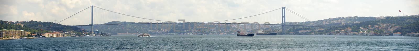Panoramic view of Ataturk suspension bridge spanning the Bosphorus river in Istanbul, Turkey against a blue sky