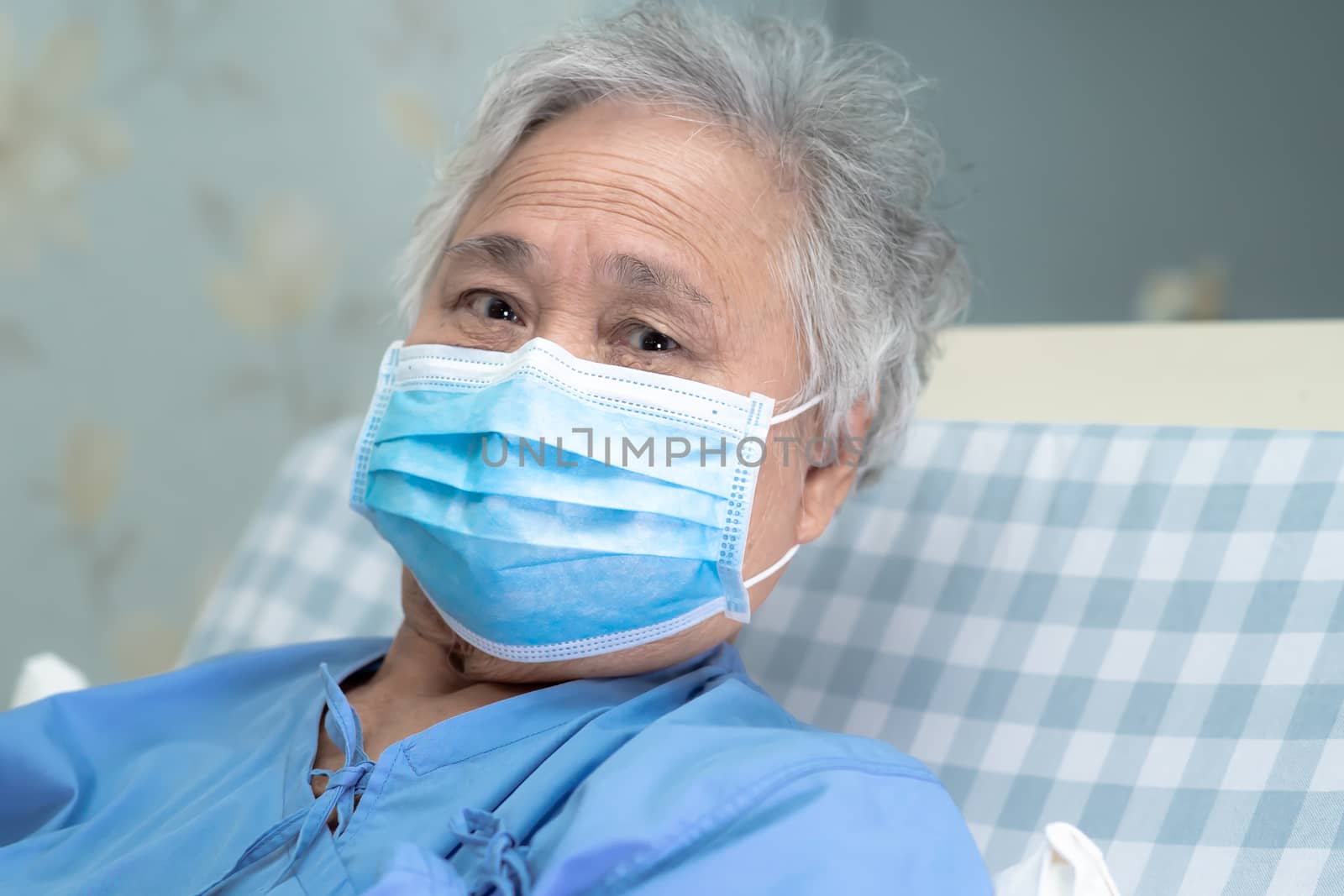 Asian senior or elderly old lady woman patient wearing a face mask to protect coronavirus and while sitting on bed in nursing hospital ward : healthy strong medical concept