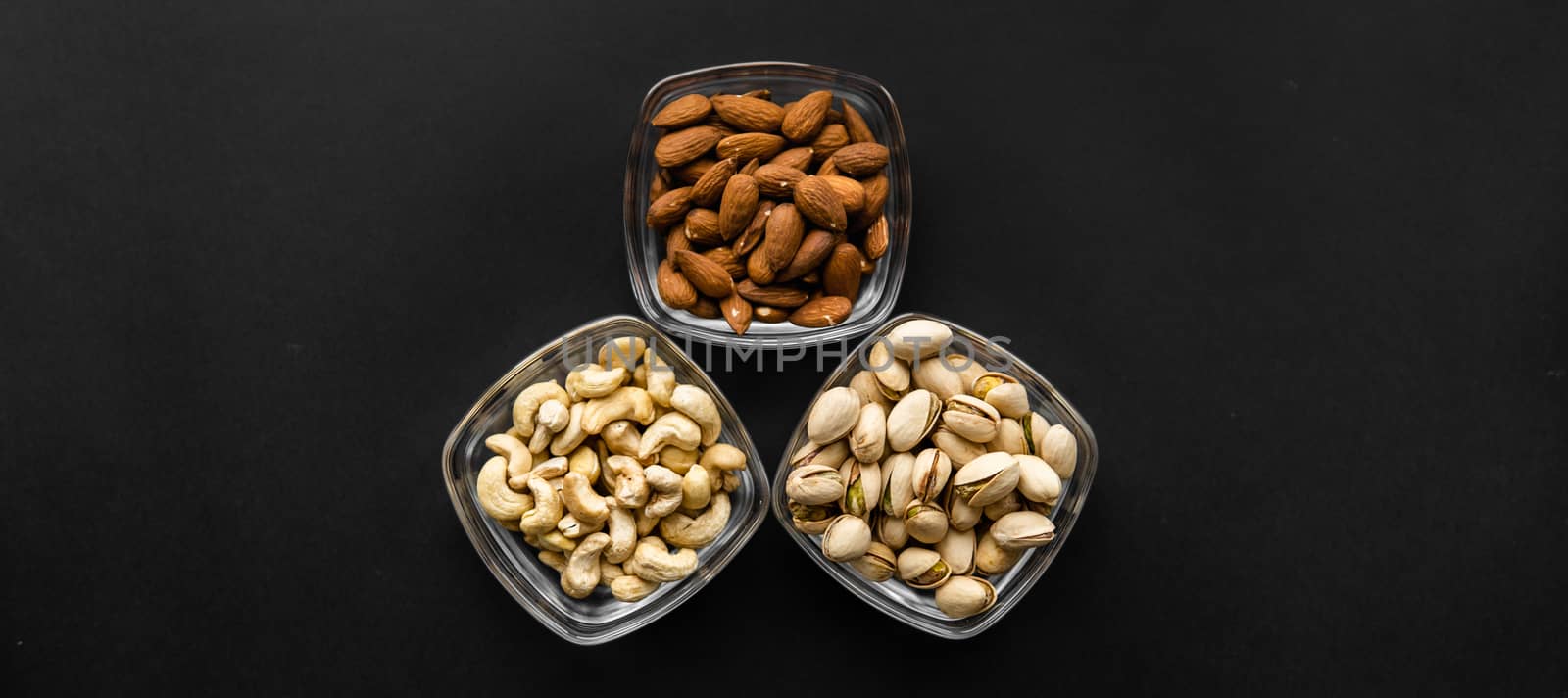 Almond, pistachio and cashew in a small plates which standing on a black table. Nuts is a healthy vegetarian protein and nutritious food. by vovsht