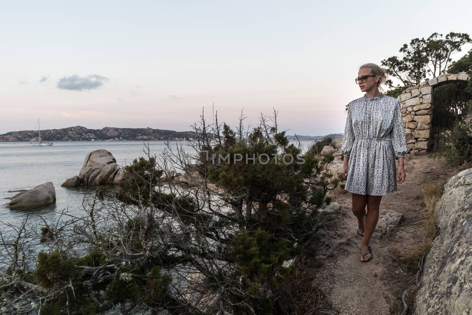 Beautiful woman in luxury summer dress enjoying peaceful seascape of Porto Rafael bay at Mediterranean sea of Costa Smeralda, Sardinia, Italy at dusk.