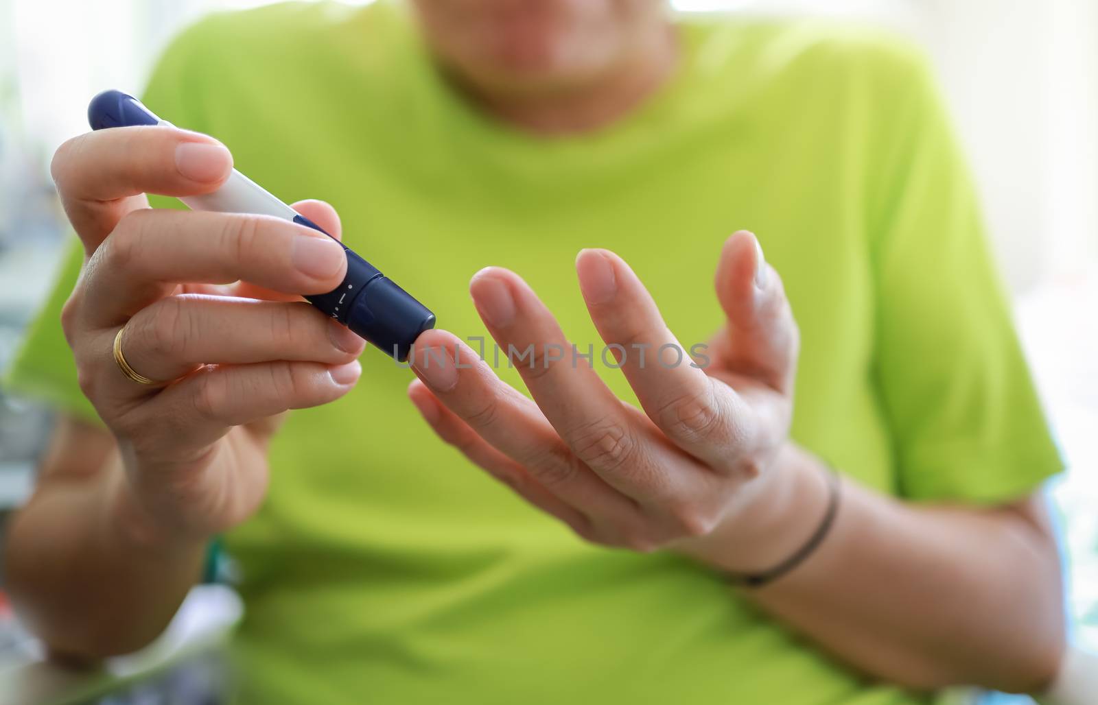 Close up of man hands using lancet on finger to check blood suga by mthipsorn