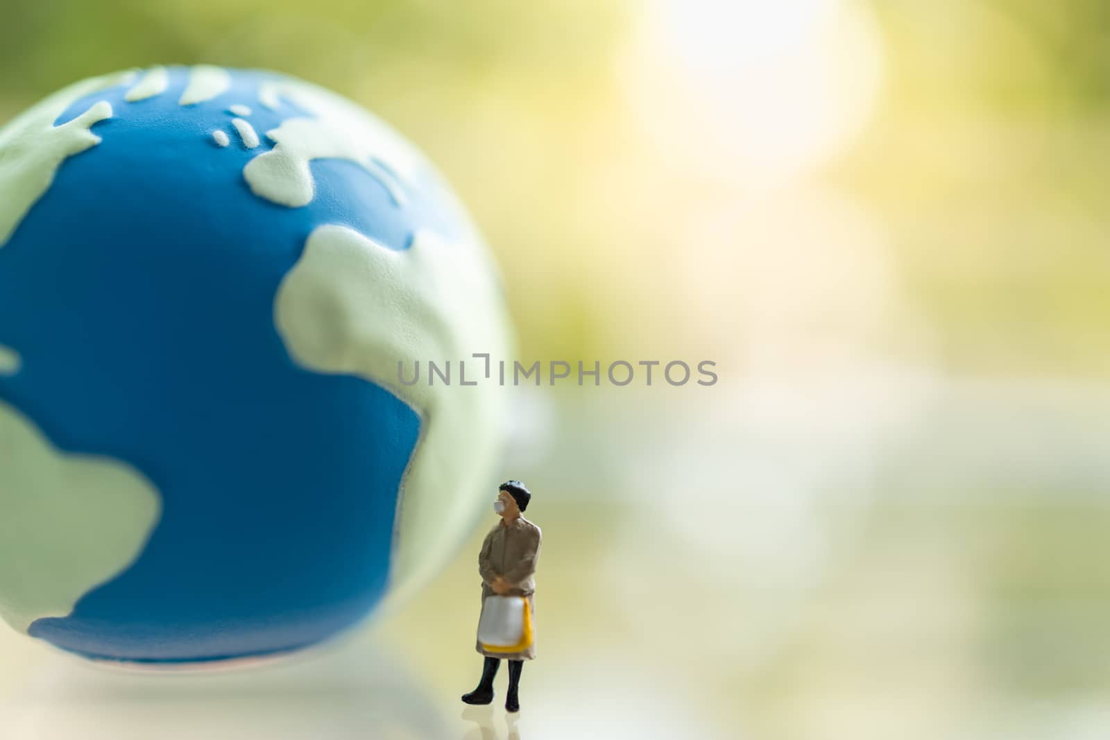 Global Healthcare, Coronavirus, Covid-19 Protection Concept. Business woman miniature figure people wearing face mask with handbag standing with mini world ball wuth green nature background and copy space.