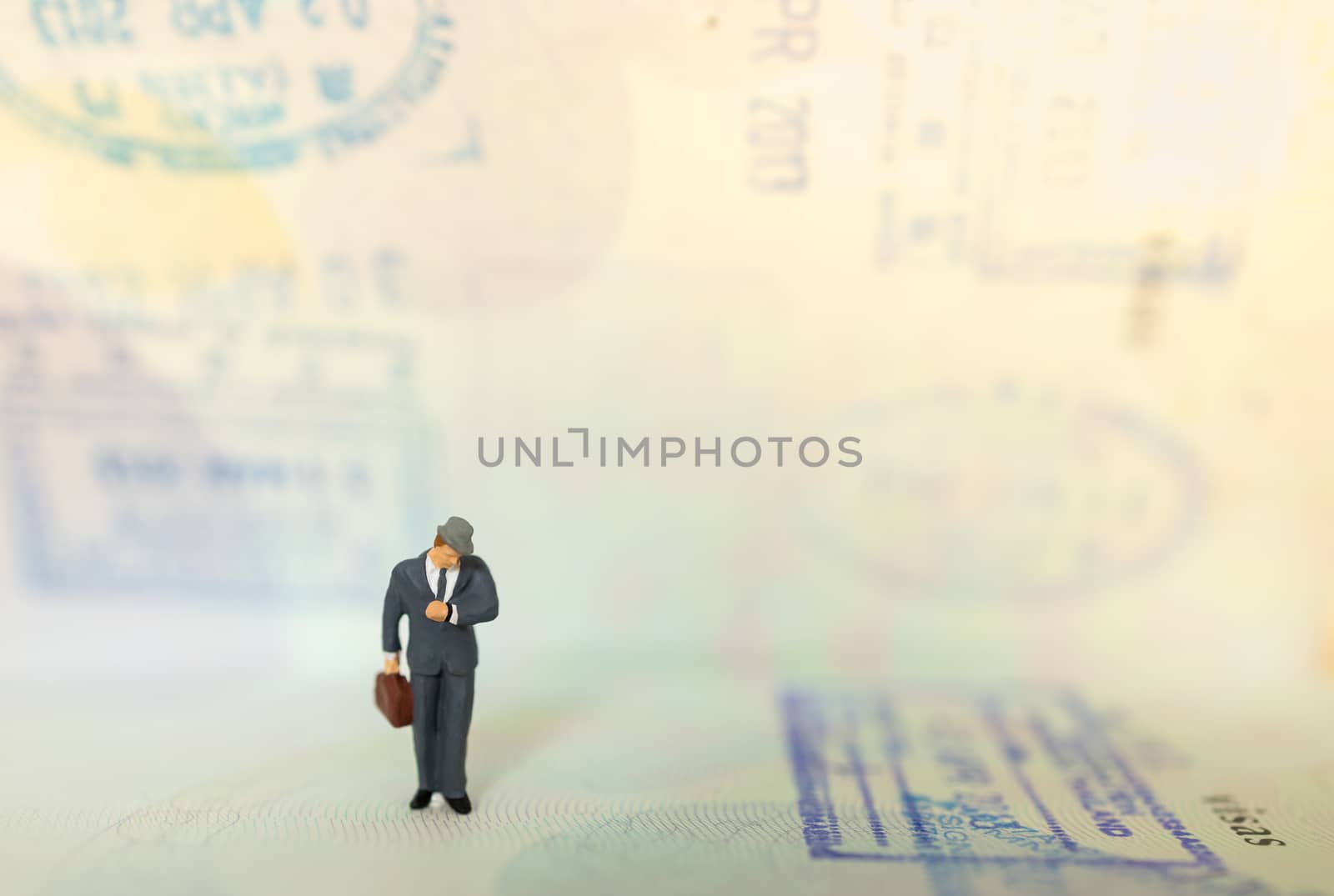Time, Travel and planning concept. Businessman miniature figure people with suitcase standing and look to wrist watch on passport with immigration stamped and copy space.