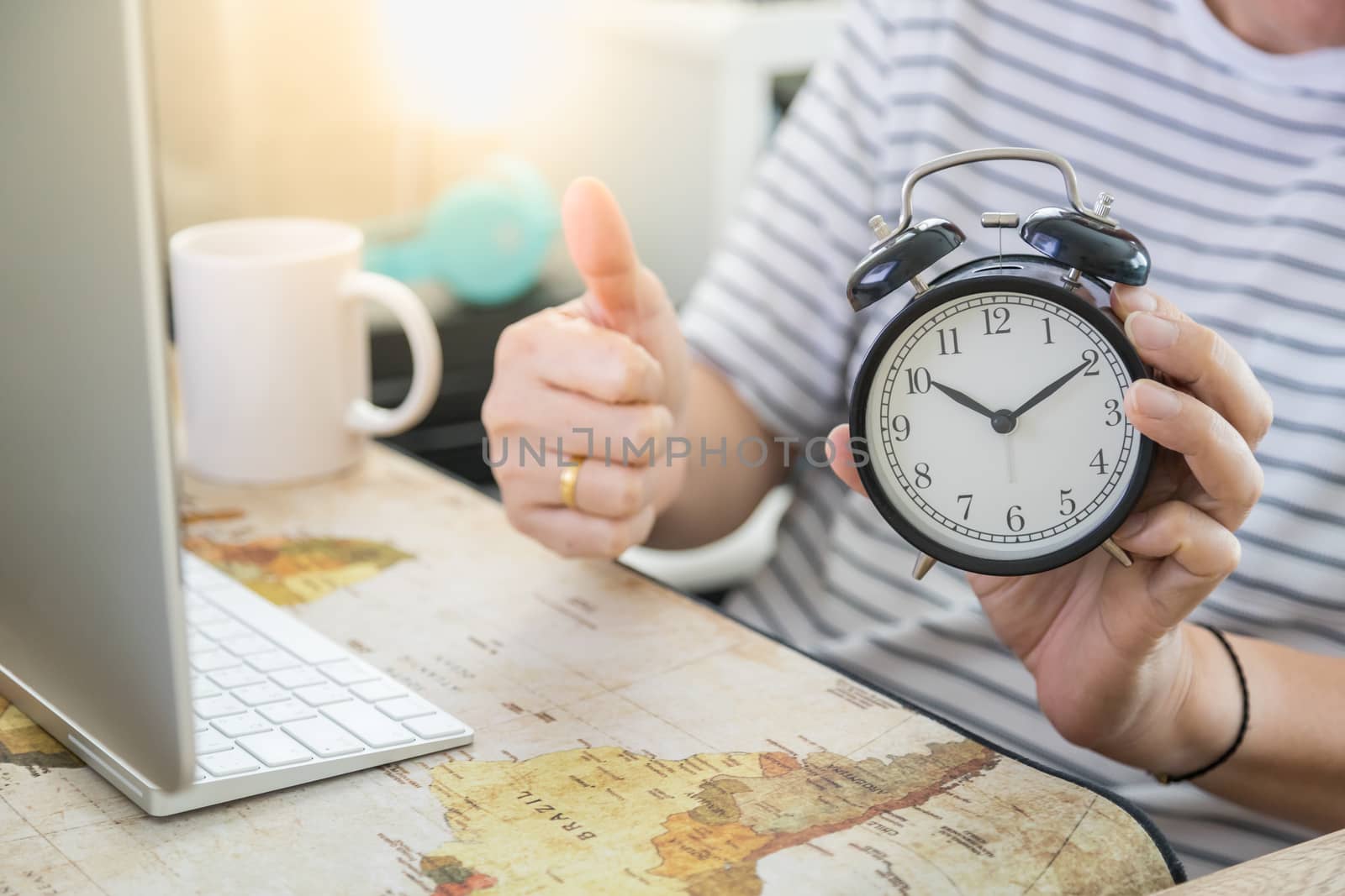 Business, Time, Technology, Work from home, Shelter in place Concept. Man hand holding vintage alarm clock with thumb up with desktop computer and white mug cup of coffee in his house.
