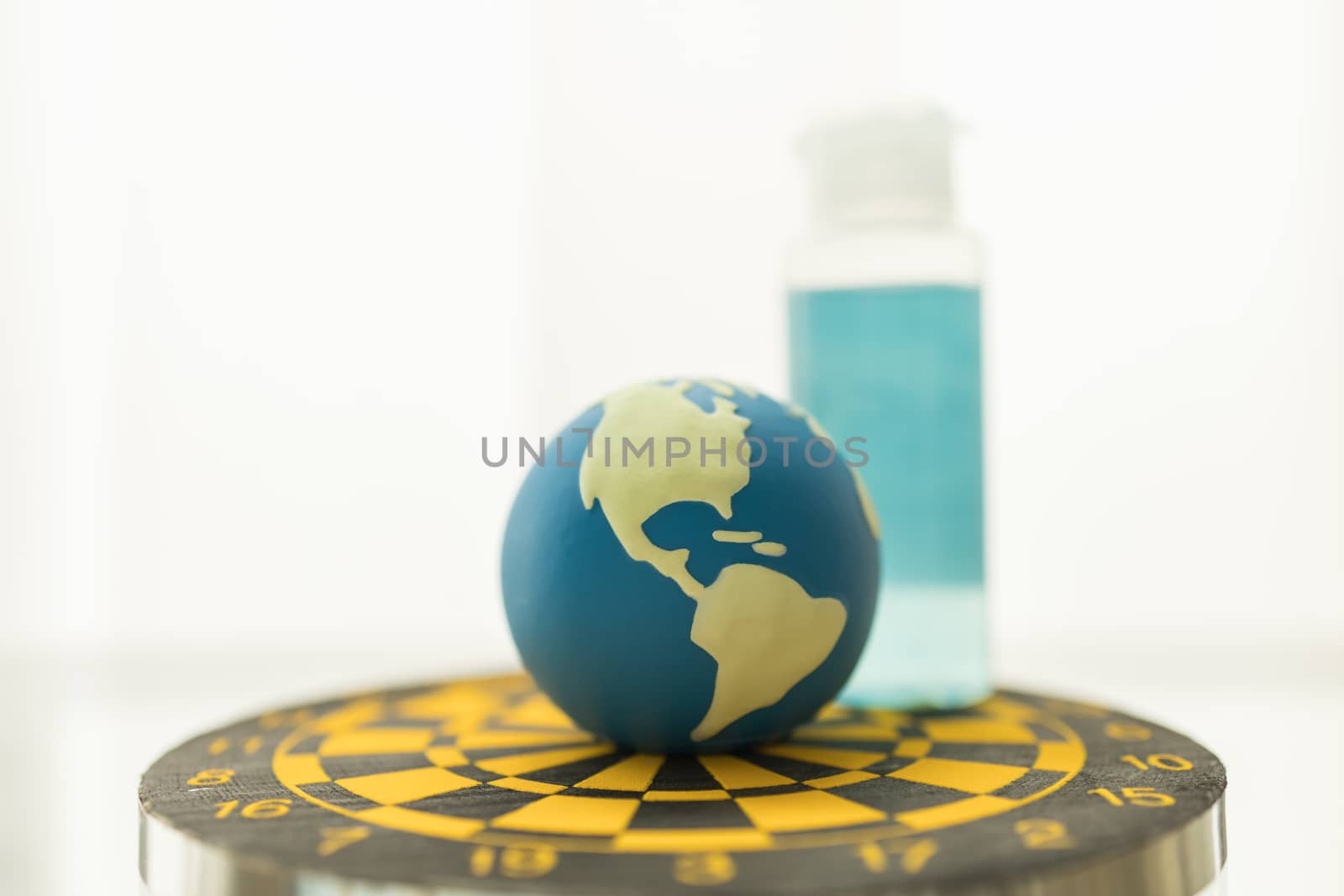 Global Healthcare, Coronavirus, Covid-19 Protection, Planning and Target Concept. Close up of mini world ball with mini bottle alcohol gel sanitizer on yellow and black dartboard