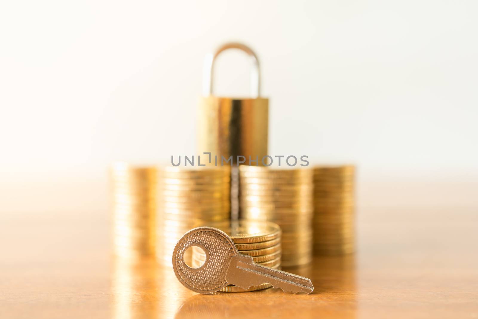 Money, Finance, Retirement and Security Concept. Close up of piece key with stack of gold coins and master key lock on wooden table with copy space.