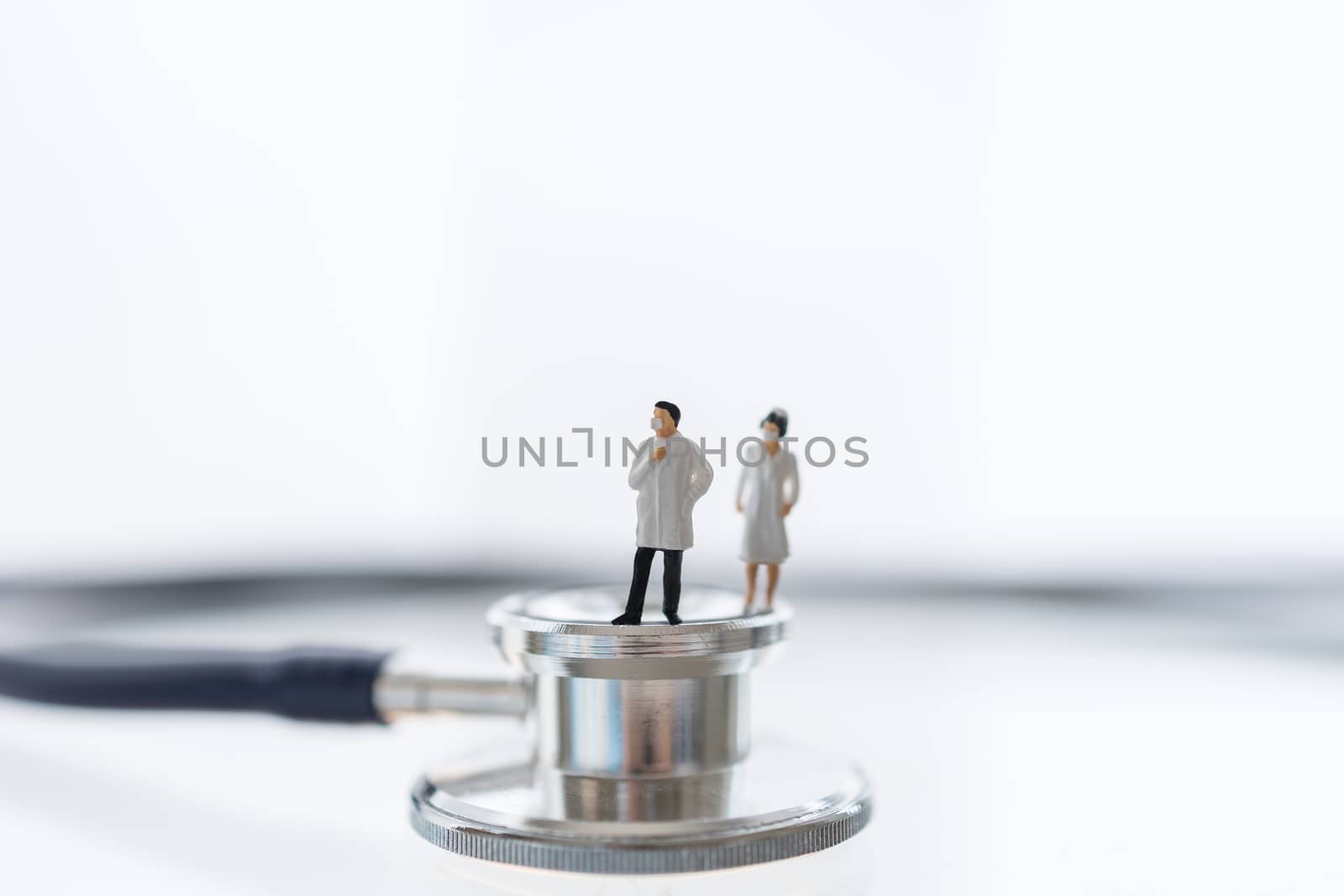 Global Healthcare, Coronavirus, Covid-19 Protection Concept. Doctor and nurse miniature figure people wearing surgical face mask standing on Stethoscope with white background.