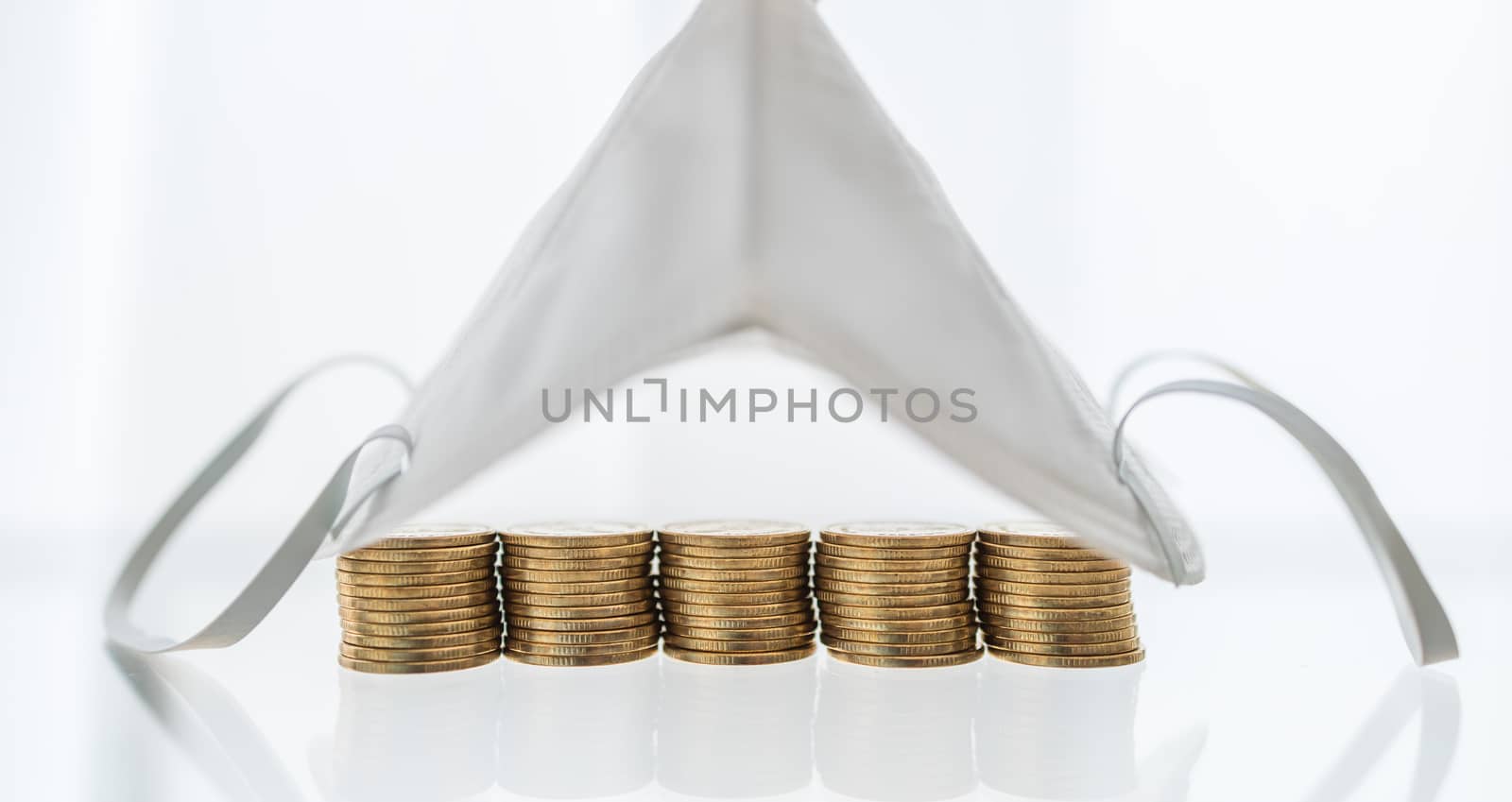 Money, Business, Healthcare in Cornavirus (COVID-19) Situation Concept. Stack of gold coins under N95 face mask on white background with copy space.