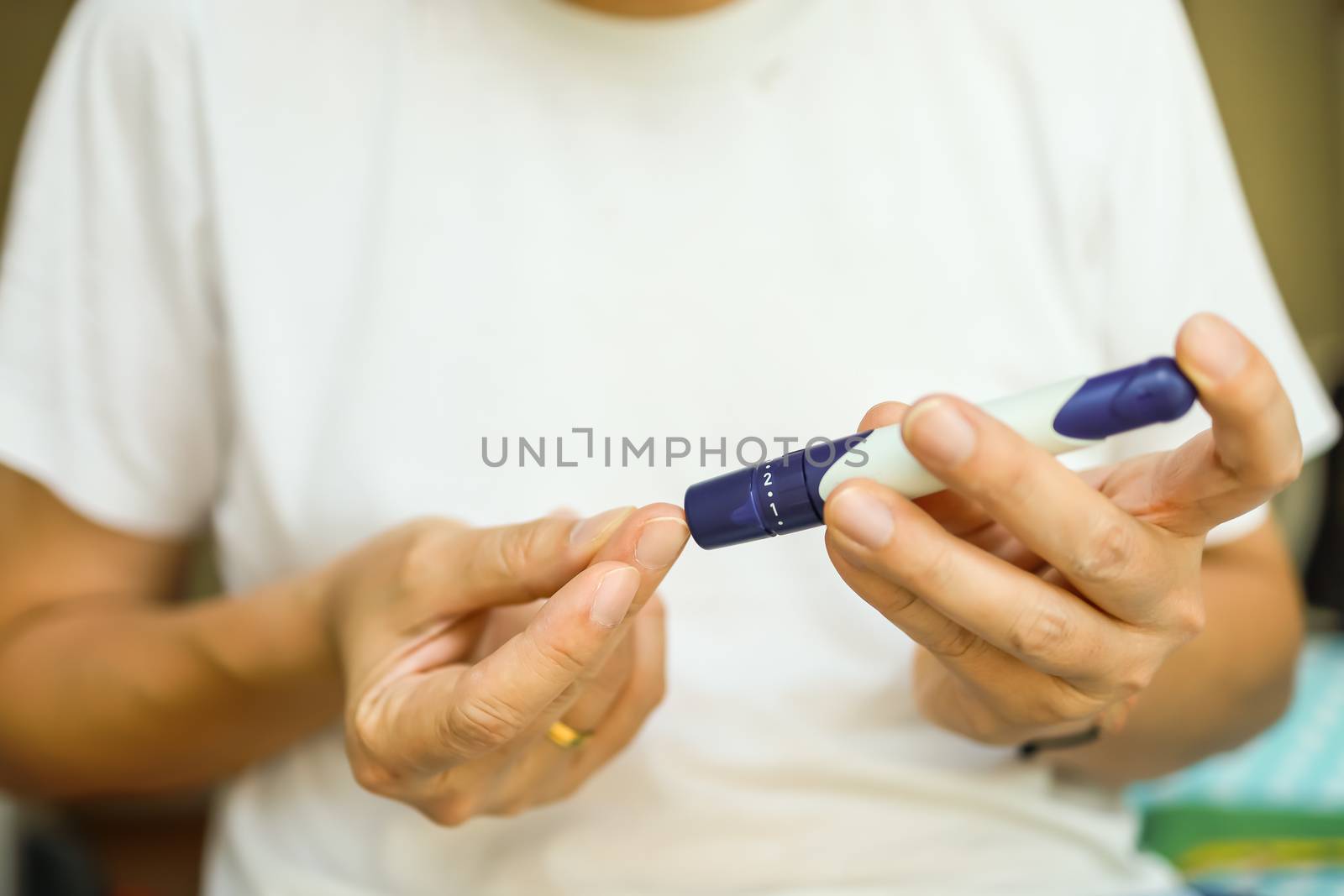 Close up of man hands using lancet on finger to check blood sugar level by Glucose meter in bedroom in the morning. Use as Medicine, diabetes, glycemia, health care and people concept.