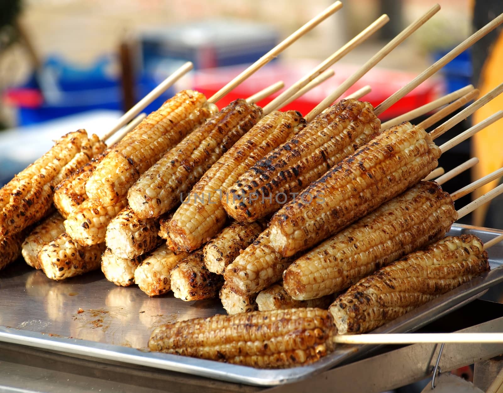 An outdoor vendor displays barbecued corn on the cob
