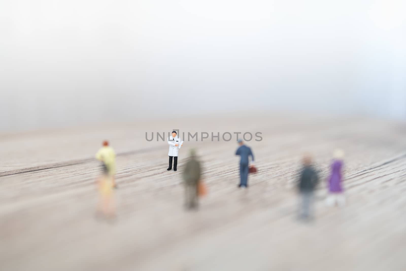 Healthcare Concept. Doctor miniature figure with patient clipboard with group of people with social distancing on wooden table and copy space