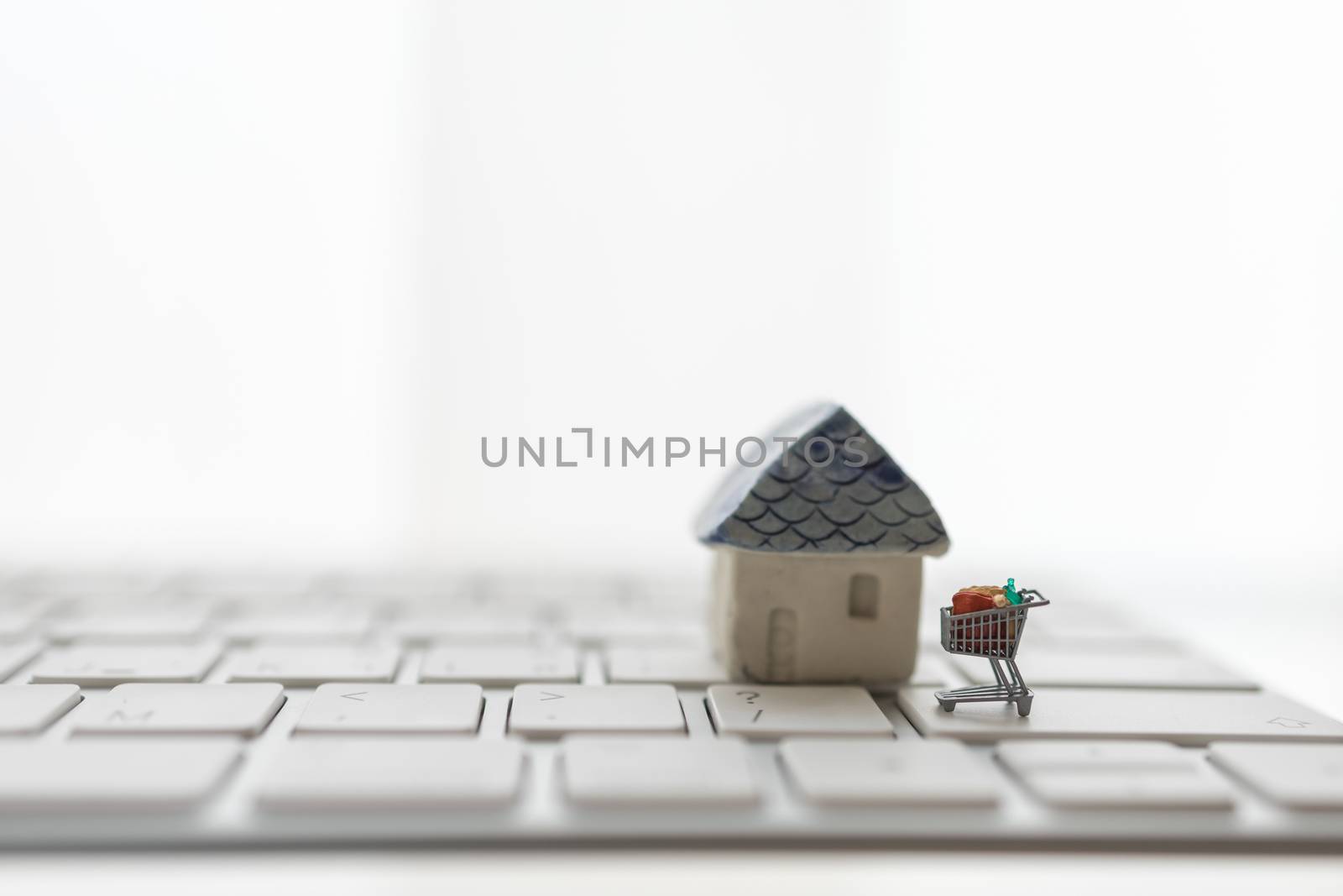 Online, E-Commerce and Technology concept.  Close up of miniature shopping cart / trolley on computer keyboard with mini house toy on white background.