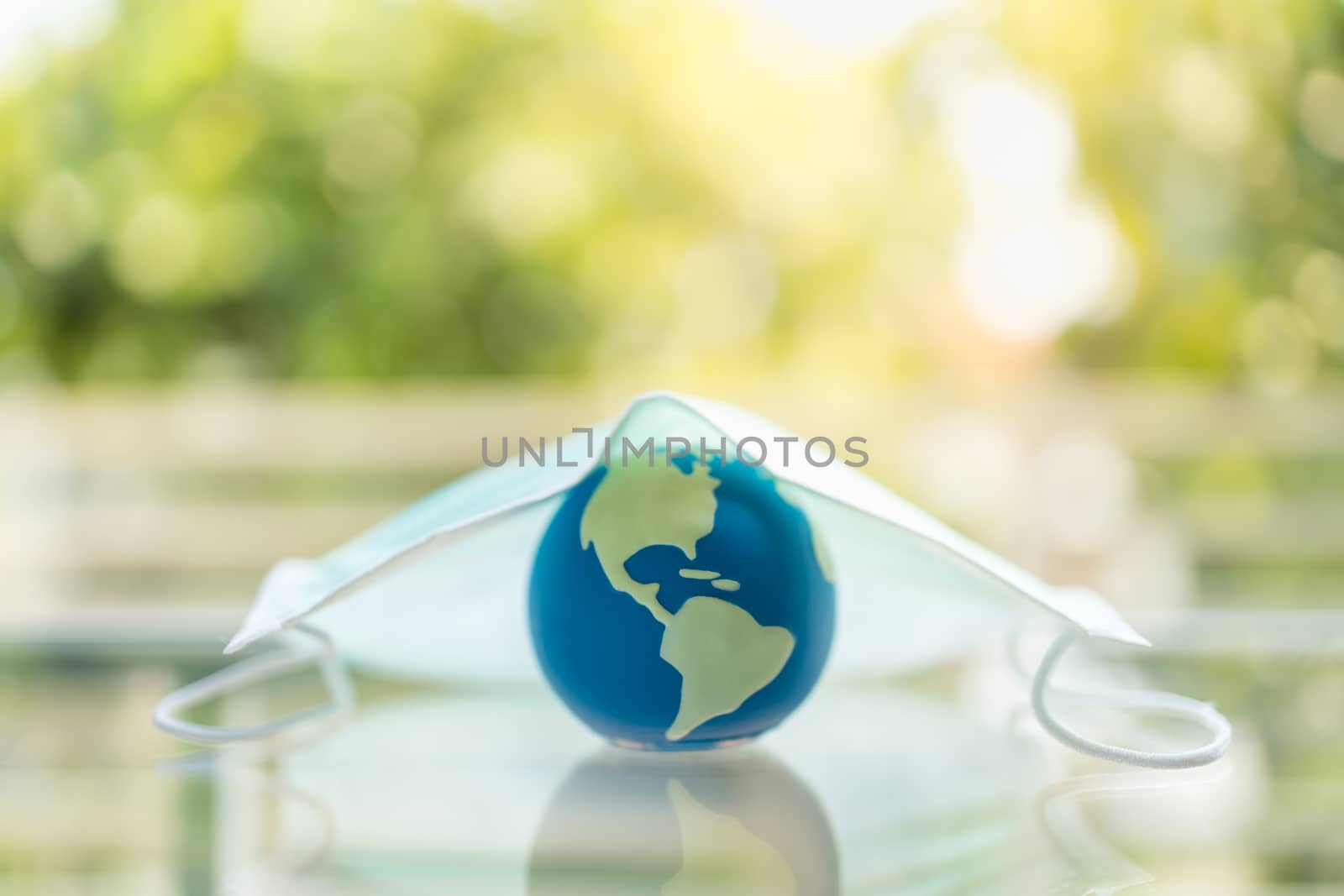 Global Healthcare, Coronavirus, Covid-19 Protection Concept. Close up of mini world ball under surgical face mask with green nature background and copy space.
