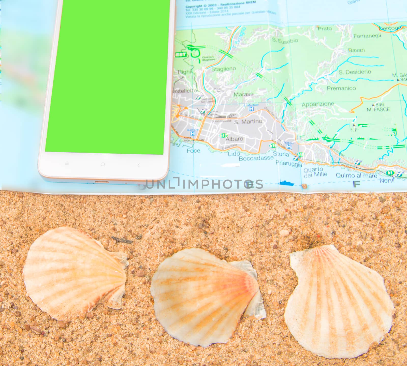 Green screen chromakey smartphone on the tourist map with shells on the sand, the phone screen can be replaced, the concept of tourism, top view.