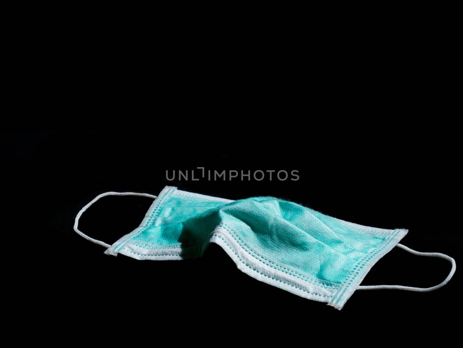 Used surgical mask place on black background with copy space, discarded mask concept. Dark tone.