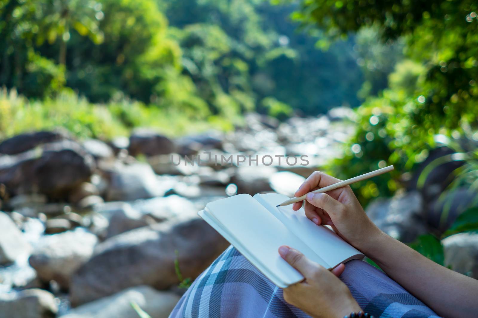 Woman hand writing down in small white memo notebook for take a note not to forget or to do list plan. by Suwant