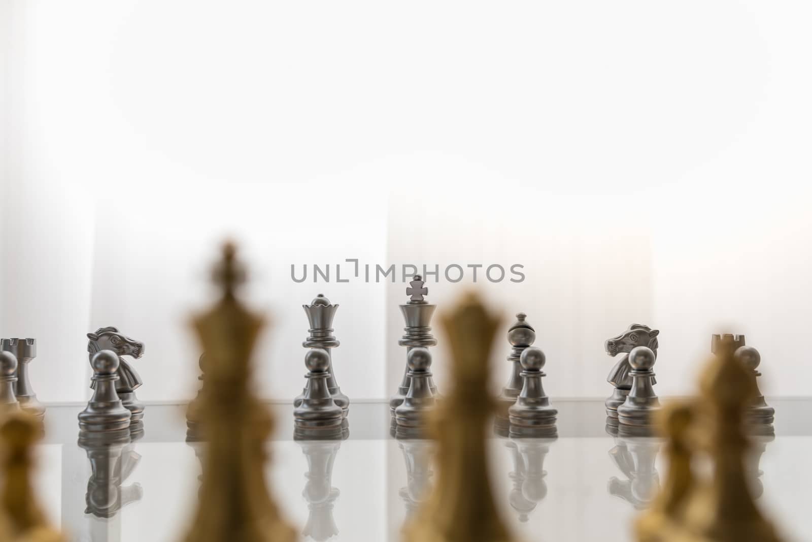 Sport board game, Business and planning concept. Closeup of King, Queen, Bishop, knight and pawn silver chess pieces face to face with gold pieces on glass table.