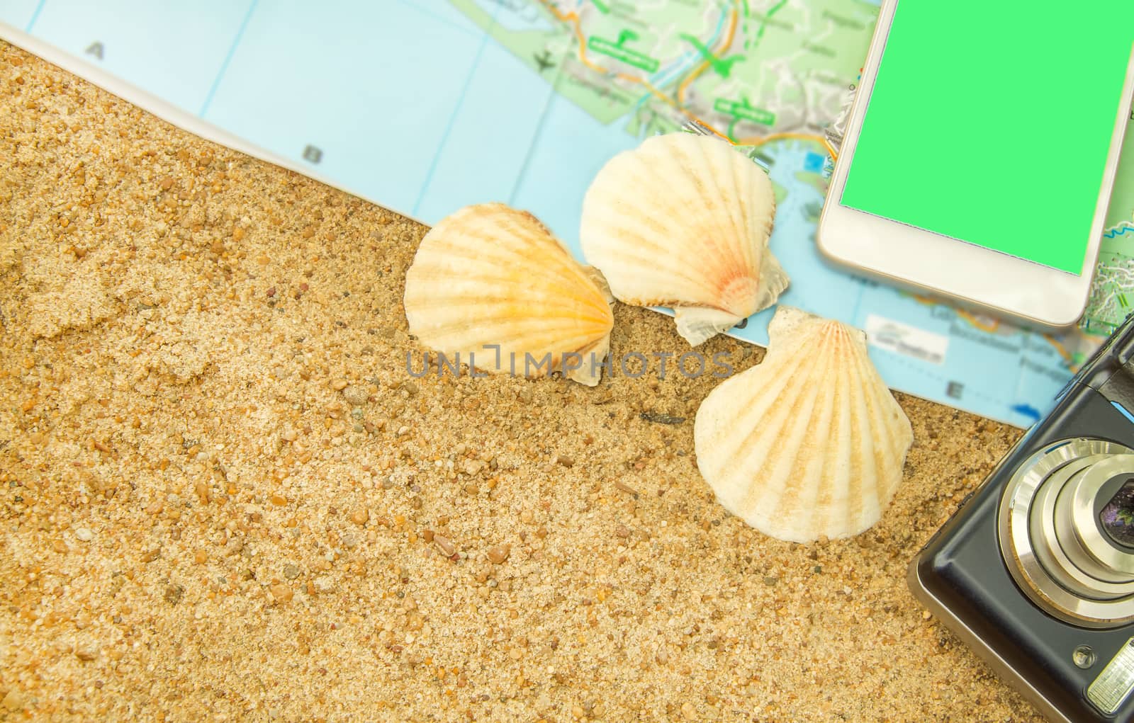 Green screen chromakey smartphone on a tourist map with a camera and shells on the sand, the phone screen can be replaced, the concept of tourism.