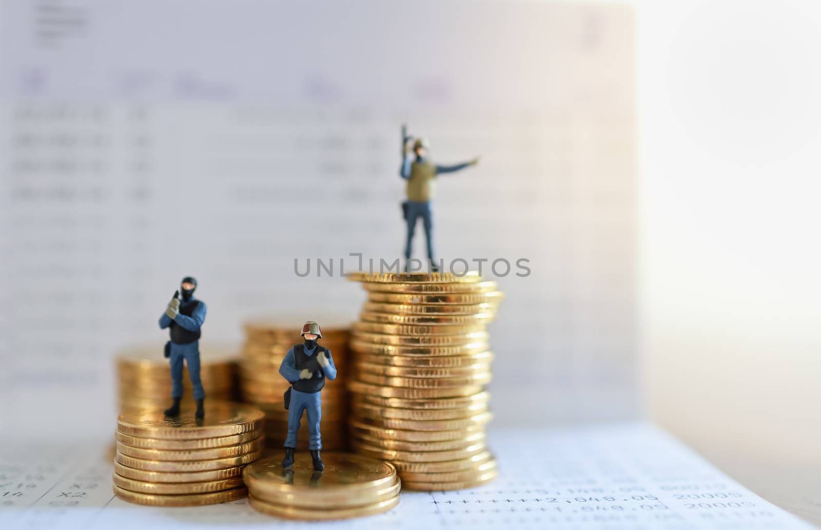 Business, Money and Security Concept. Close up of group of soldier or police miniature figure people standing and guard and protect on top stack of gold coins on bank passbook with copy space.