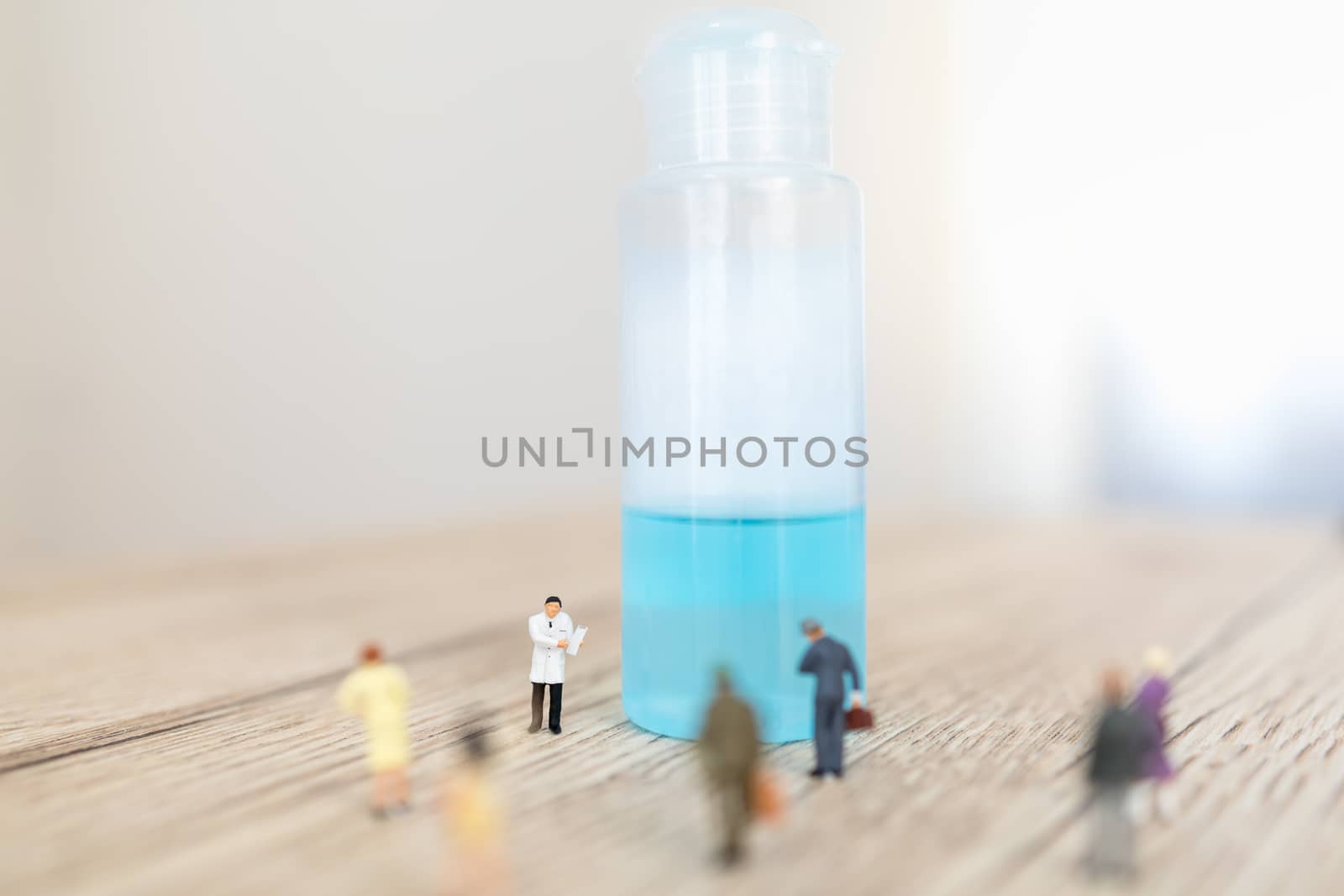 Global Healthcare, Coronavirus, Covid-19 Protection Concept. Doctor miniature figure people with patient clipboard standing with alcohol gel sanitizer with group of people on wooden table.