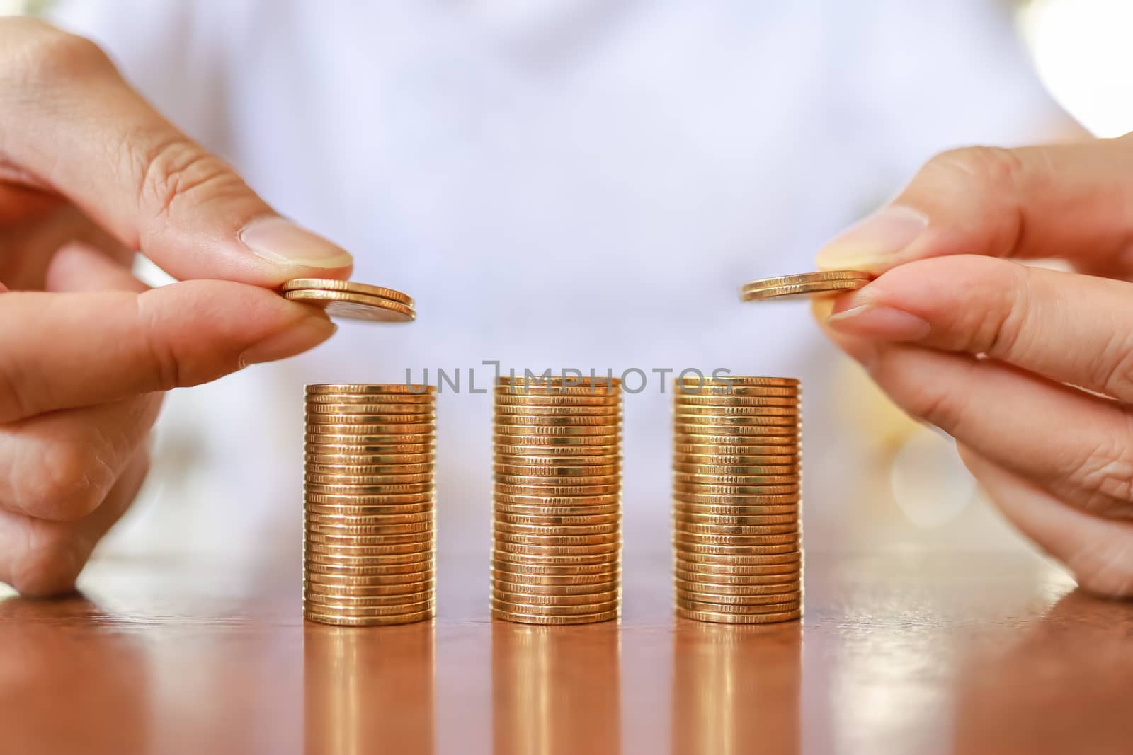 Business, Money, Finance, Secure and Saving Concept. Close up of two man hand holding and put coins to top of stack of gold coins on wooden table.