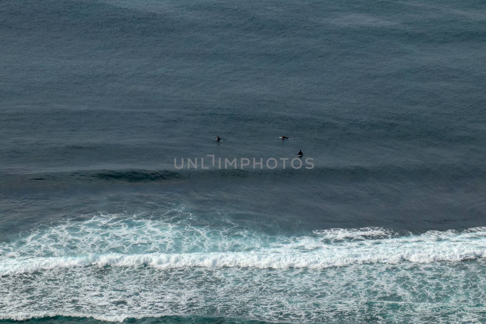 Young surfers sitting on surfboards waiting for the right wave. A young man lies on the surfboard and is spending time talking to other friends. Waves turn into sea foam as they break off the coast.