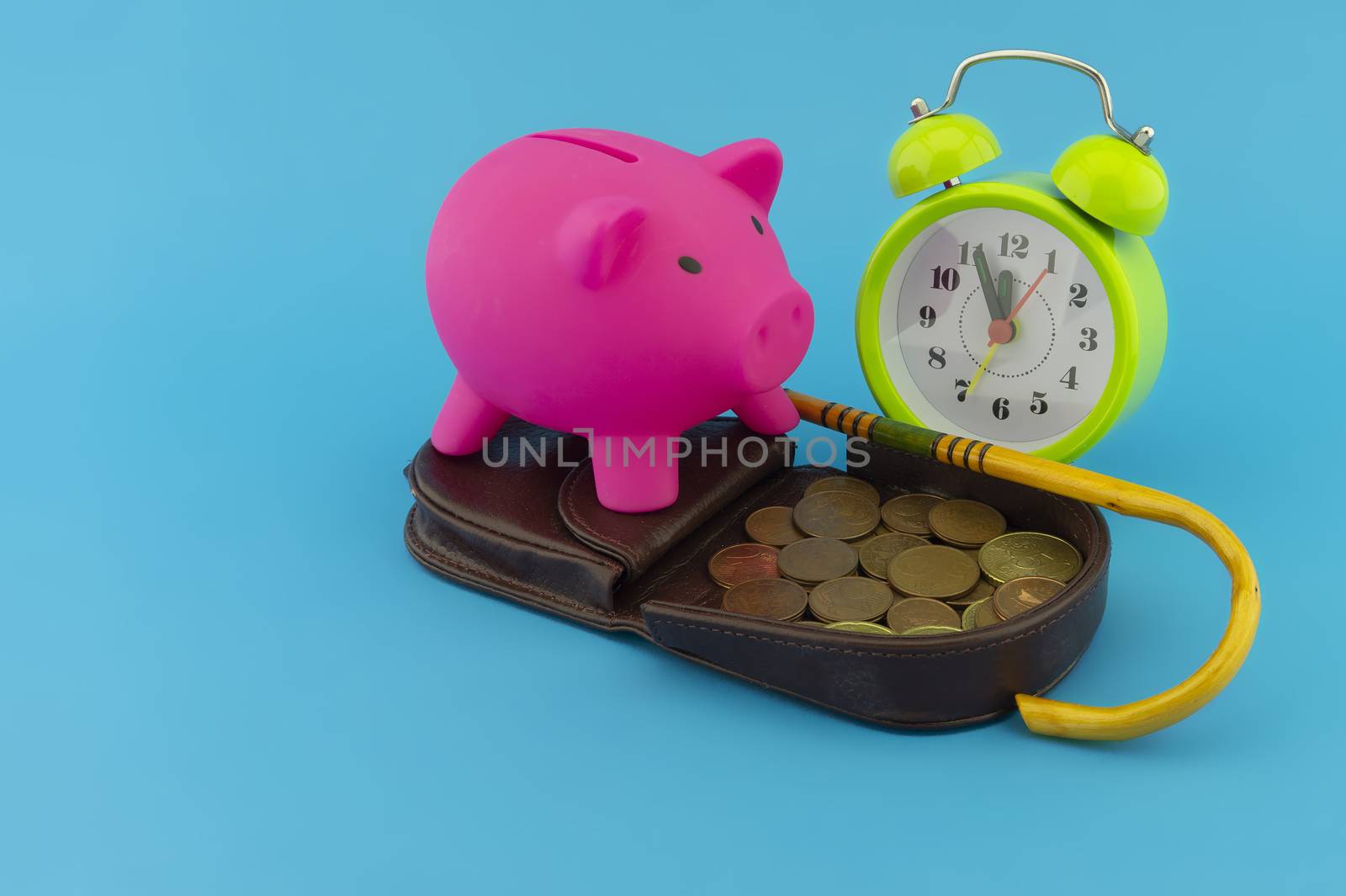 Saving for old-age and retirement concept with open purse with coins, walking stick, alarm clock and piggy bank over a blue background with copy space