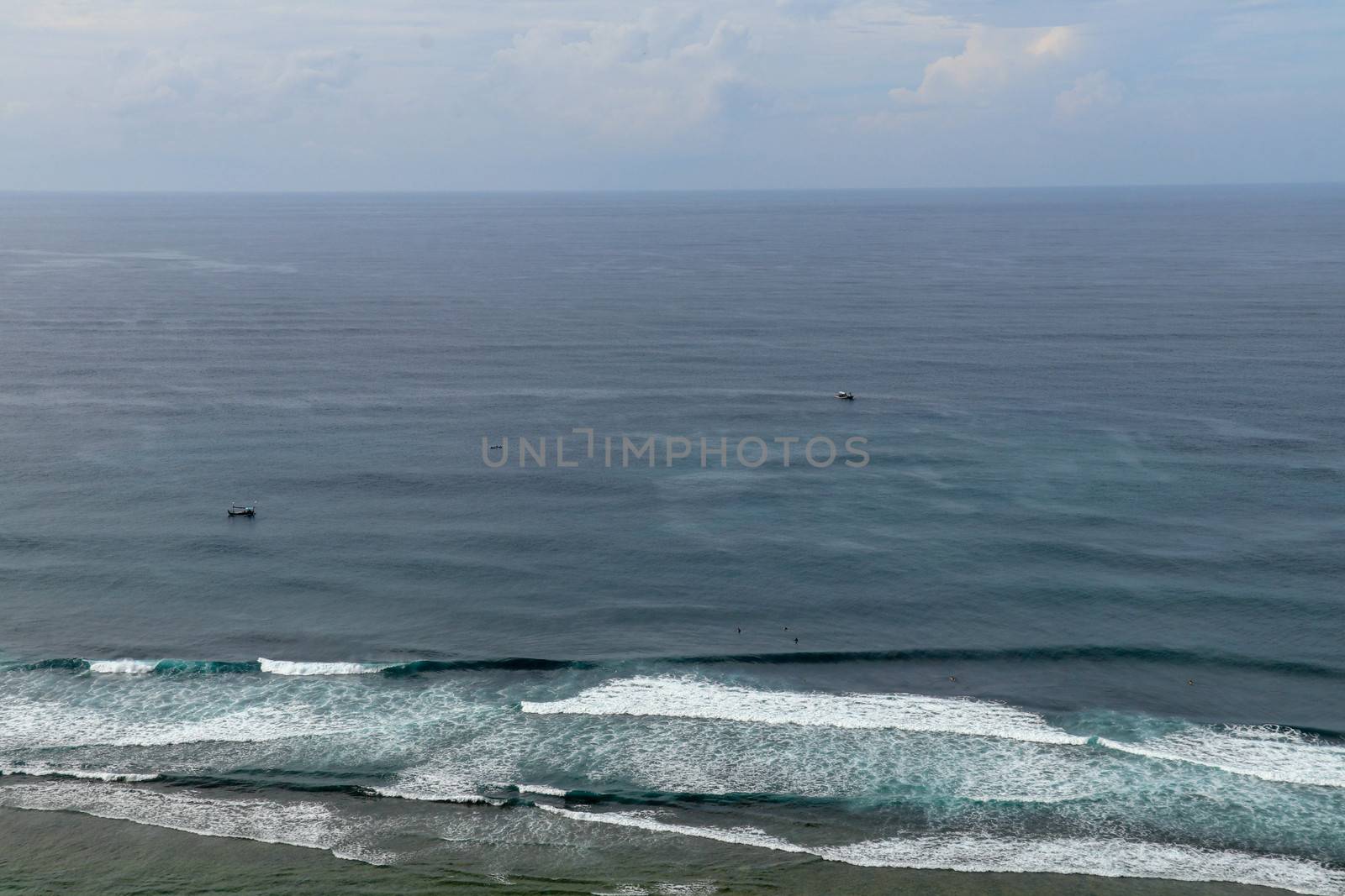 Young surfers sitting on surfboards waiting for the right wave. A young man lies on the surfboard and is spending time talking to other friends. Waves turn into sea foam as they break off the coast.