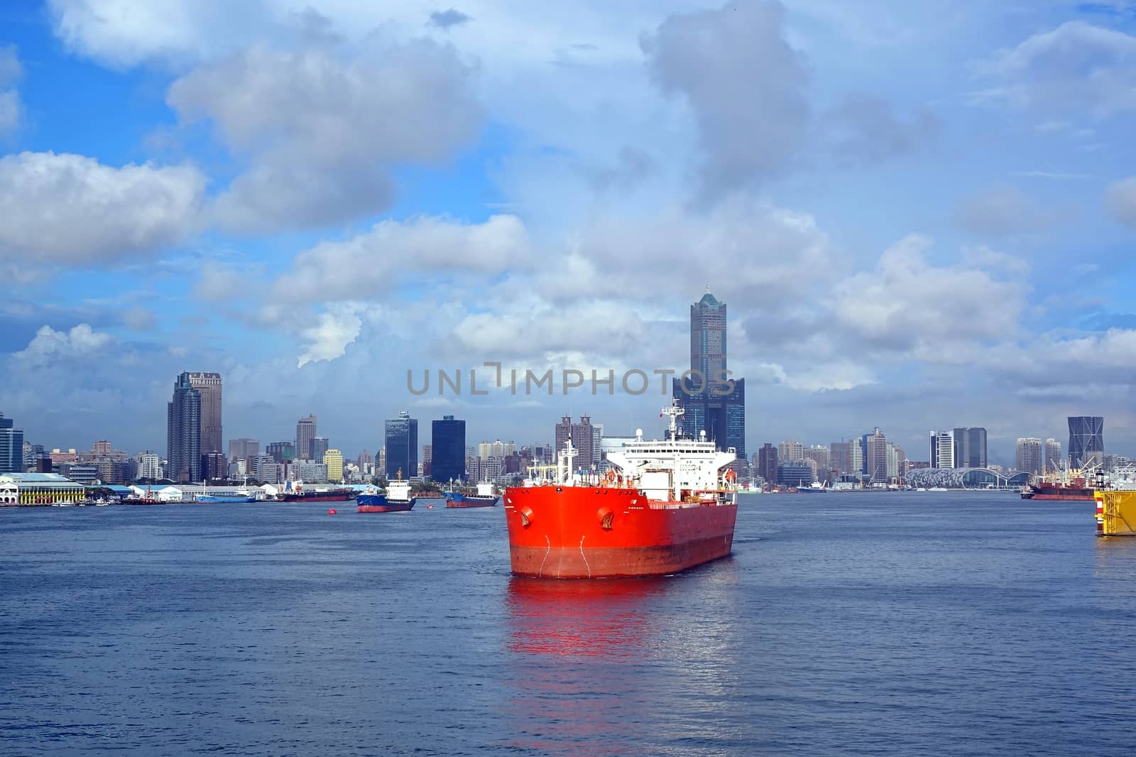 A large red oil tanker leaves Kaohsiung Port, in the background the skyline of the city.
