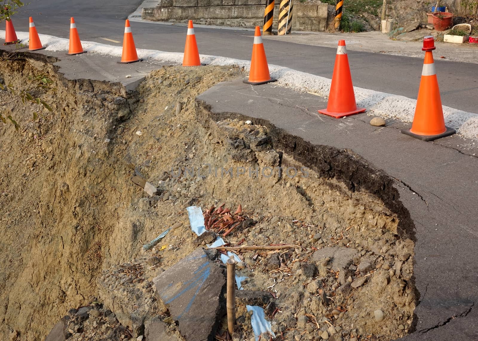 Red and white traffic cones mark a  road that has been damaged by a landslide