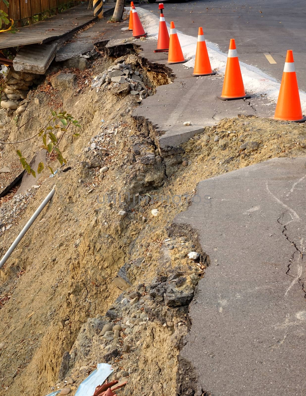 Red and white traffic cones on a  road that has been damaged by a landslide