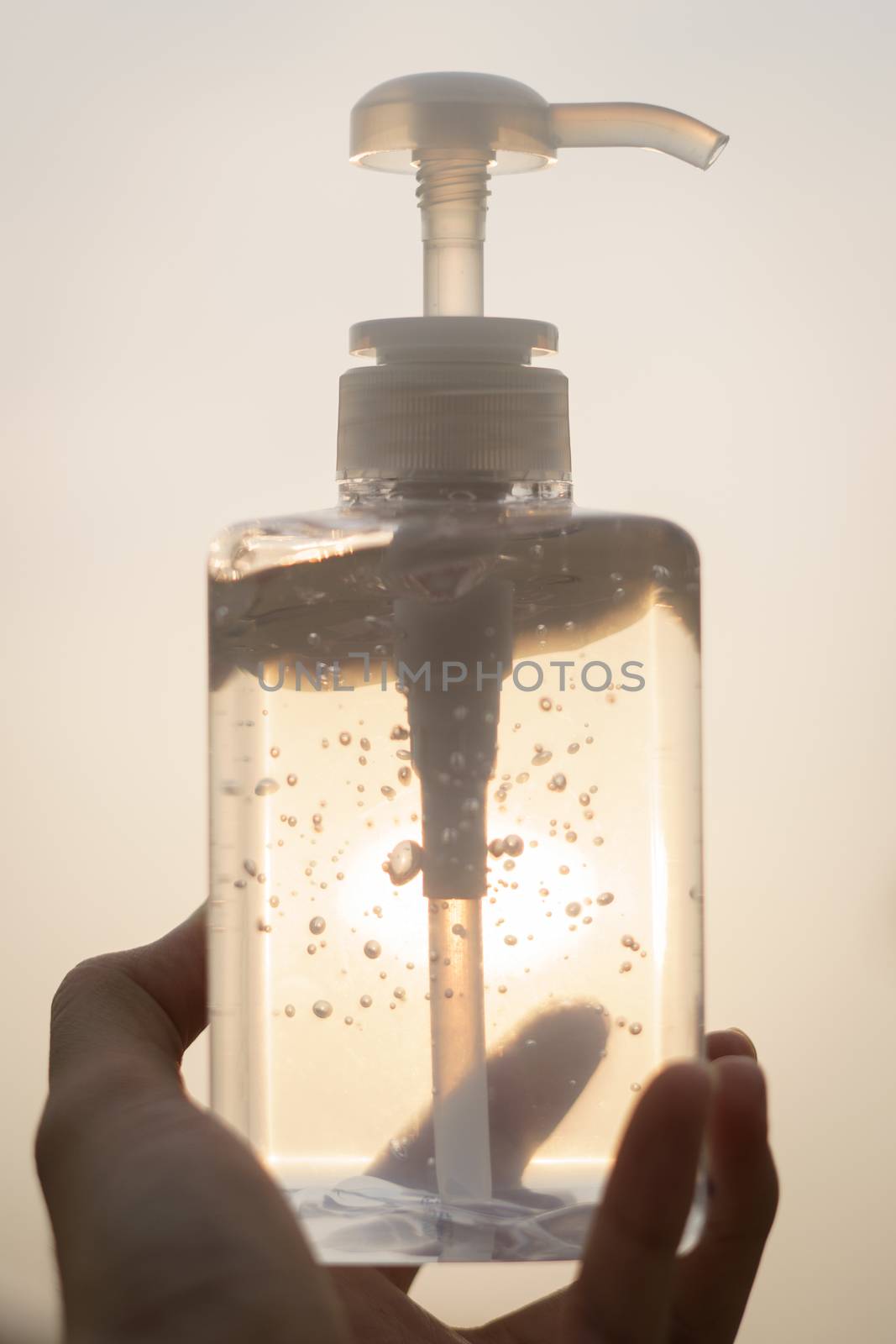 Hand with antibacterial transparent hand sanitizer gel in a plastic bottle.