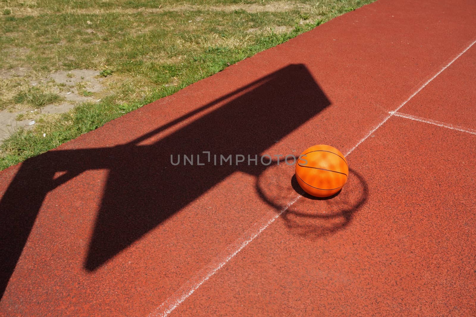 Basketball on a court placed inside the shadow of the net and goalpost in a conceptual image with copy space