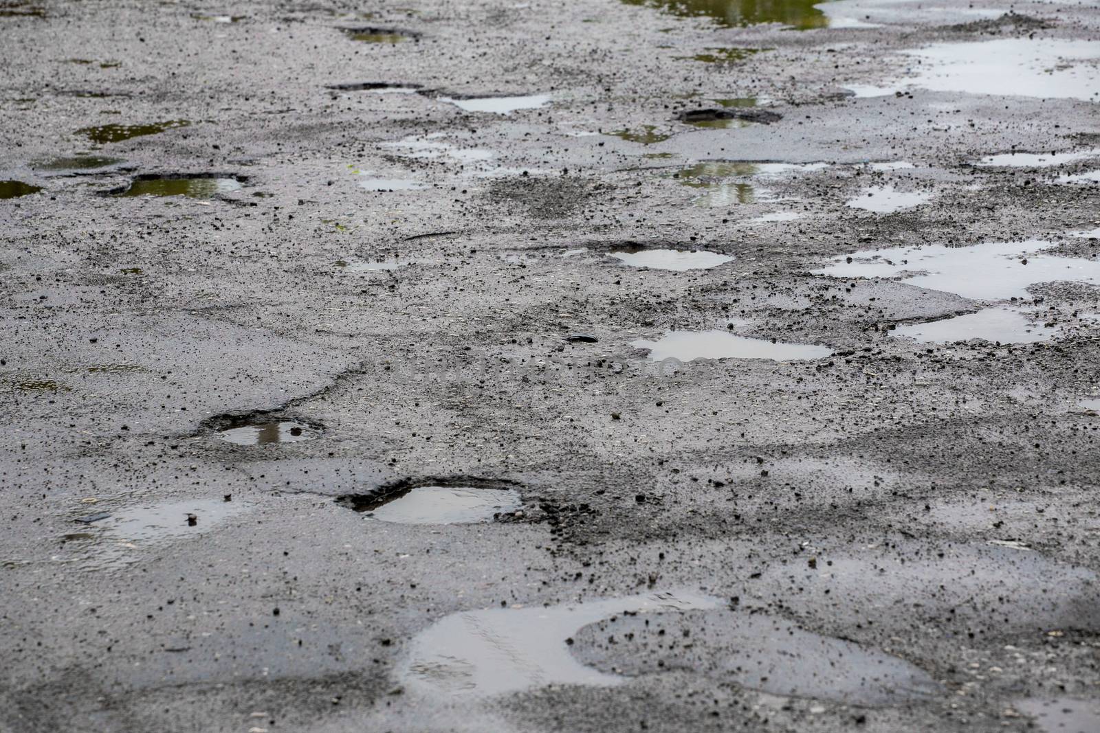 bumpy damaged road asphalt with multiple puddles after rain at summer daytime, potholes.