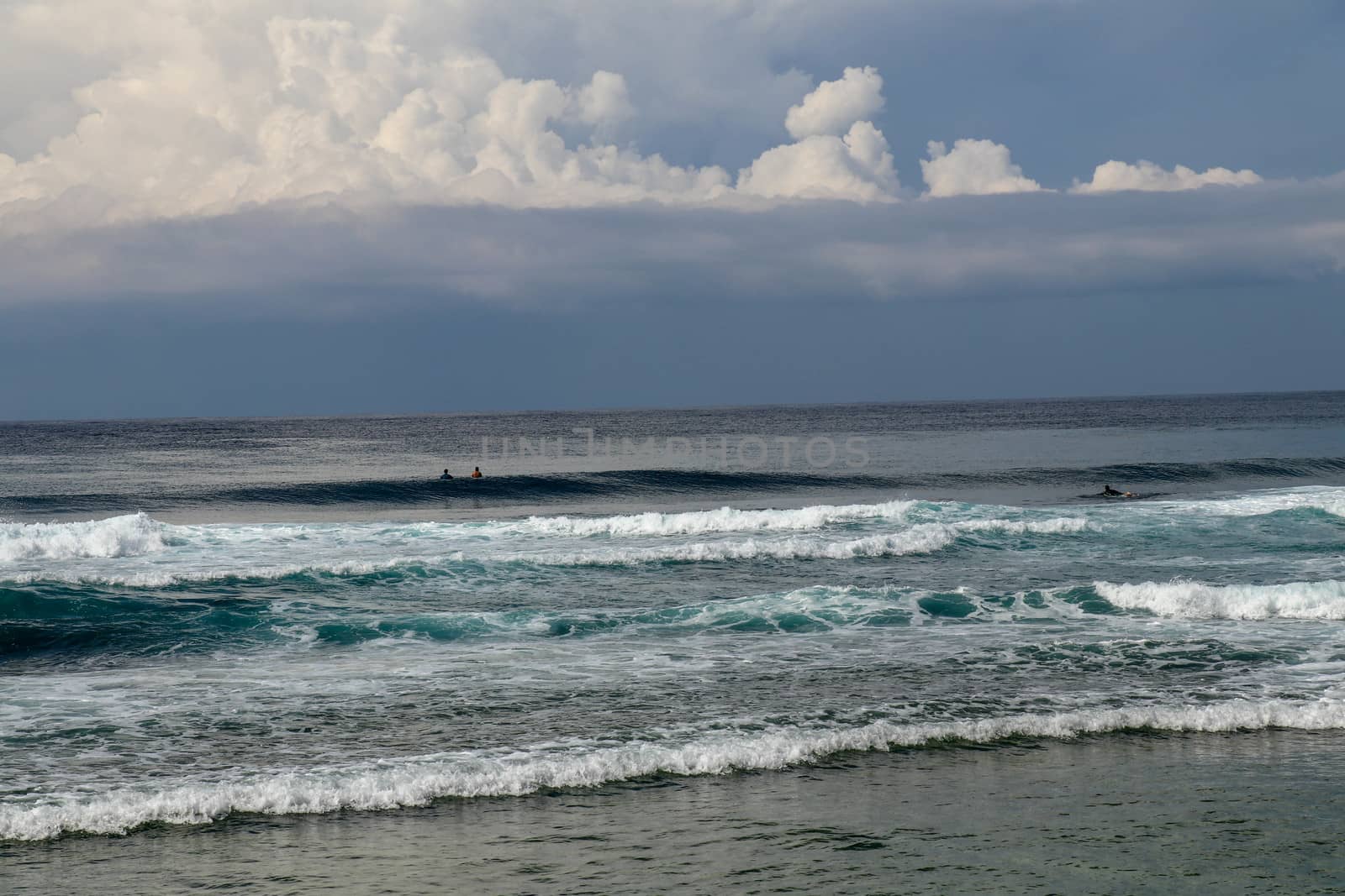 Surfers are waiting for a convenient wave on their surfboards. Tropical surfers paradise with Nyang Nyang beach on Bali island. Azure blue sky, sunny day. Wild waves are approaching the shore in rows.