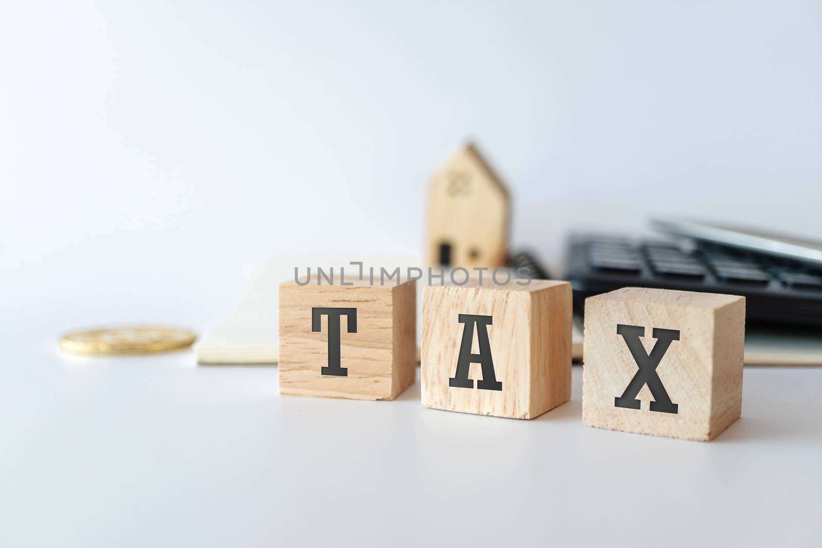 Tax word on wooden cube with objects as gold coin, calculator and mini home model behide white clean background. Business financial loan property concept.