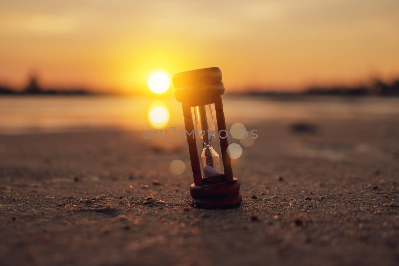 Small hourglass show time is flowing on sand beach texture background.