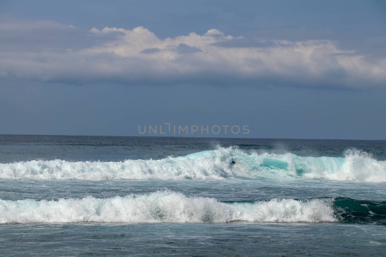 Young caucasian man surfs the ocean wave and makes a lot of splashes into the camera. Nyang Nyang Surf Spot in Bali, Indonesia. The surfer falls into the ocean waves. Man rides the wave at sunny day.