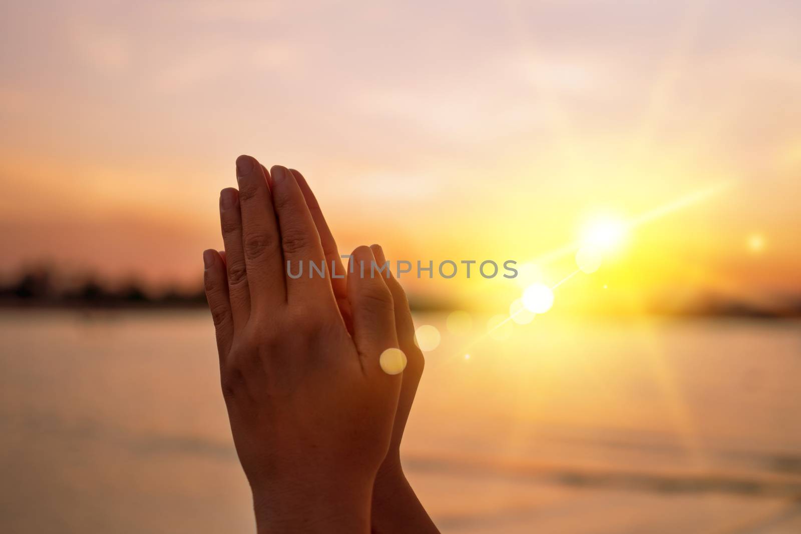 Woman hands place together like praying in front of nature blur beach sunset sky background.