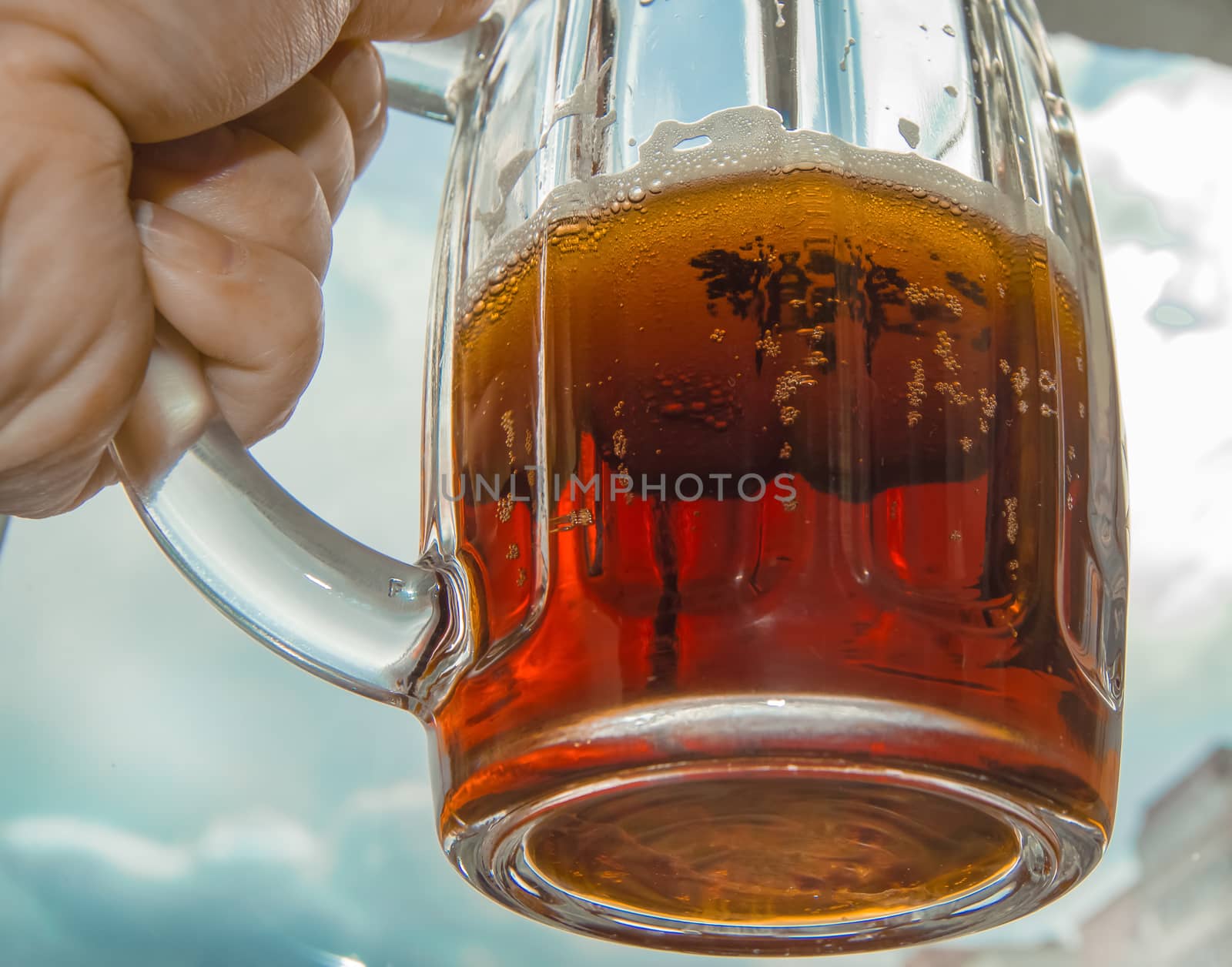 Hand with a mug of cold beer against the sky, close-up, bright light by claire_lucia