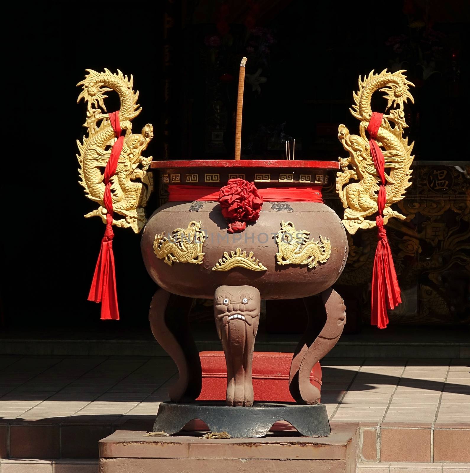A Chinese incense burner with a large burning joss stick and two golden dragon decorations
