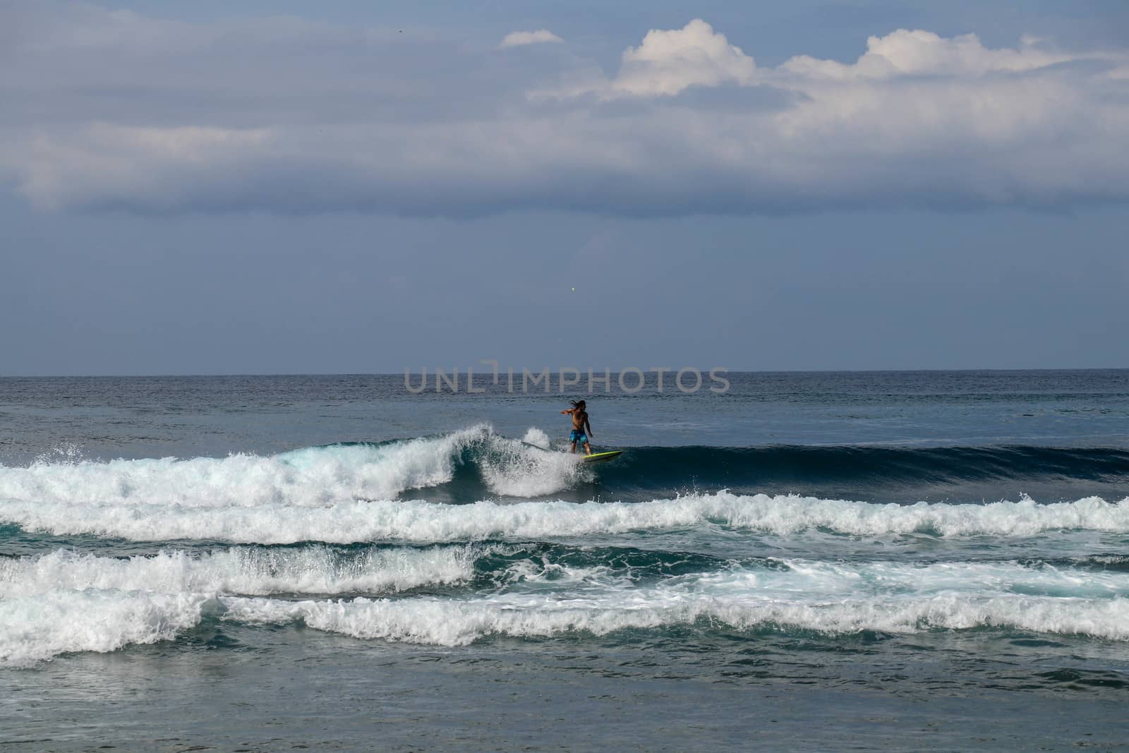 Young man sliding down a wave on a yellow surfboard. Surfer on a yellow surfboard on the crest of the wave. Young surfer learns to catch waves. First steps in surfing sport.