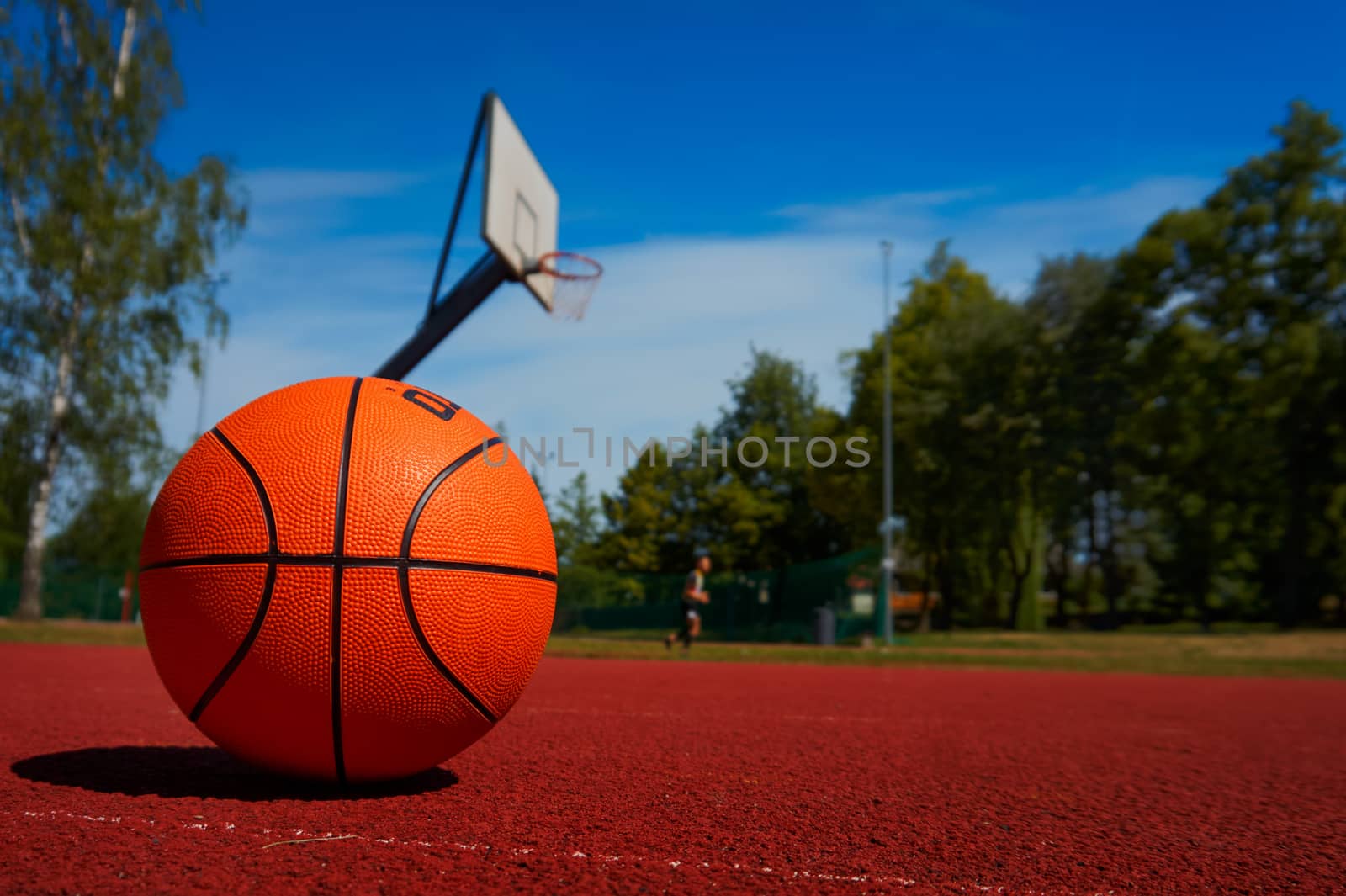 Basketball on outdoor basketball court floor against the trees and blue cloudy sky. Free copy space.
