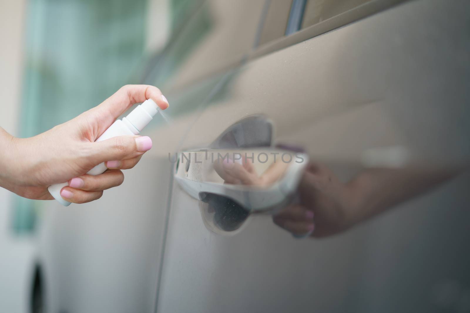 Hand hold bottle alcohol spraying disinfecting door handle of car, for corona virus or Covid-19 protection.