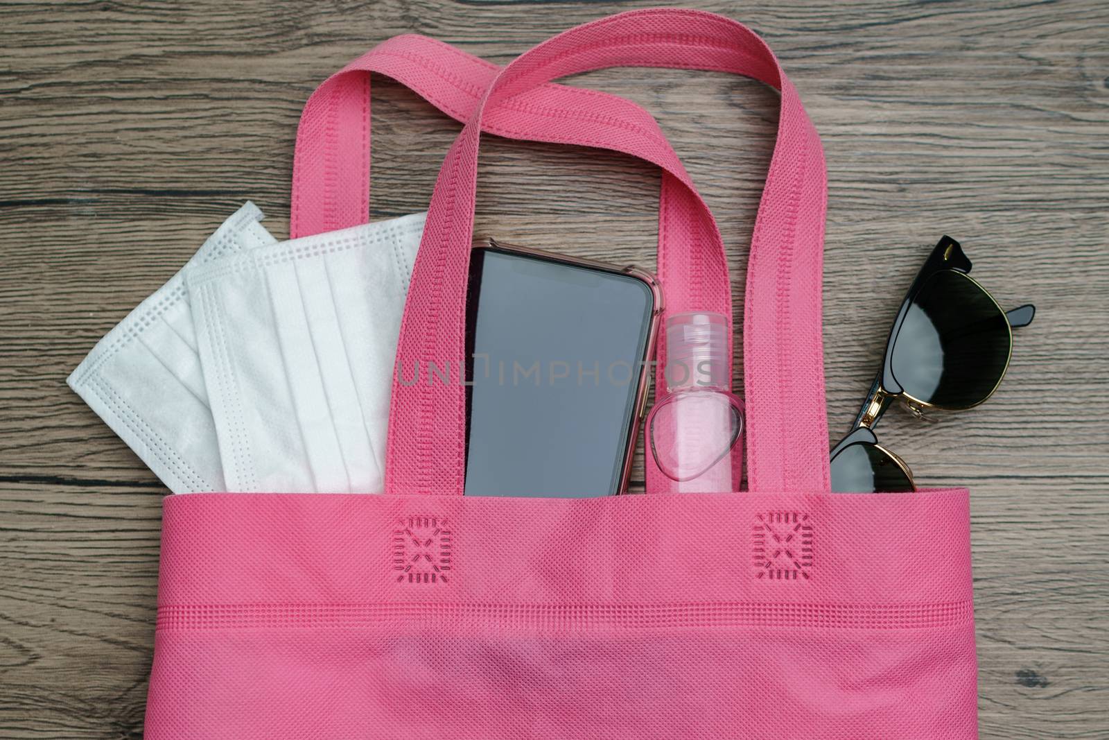 Shopping bag with must have items smart phone, protective face mask, glasses and sanitizer gel, corona virus or Covid-19 protection.