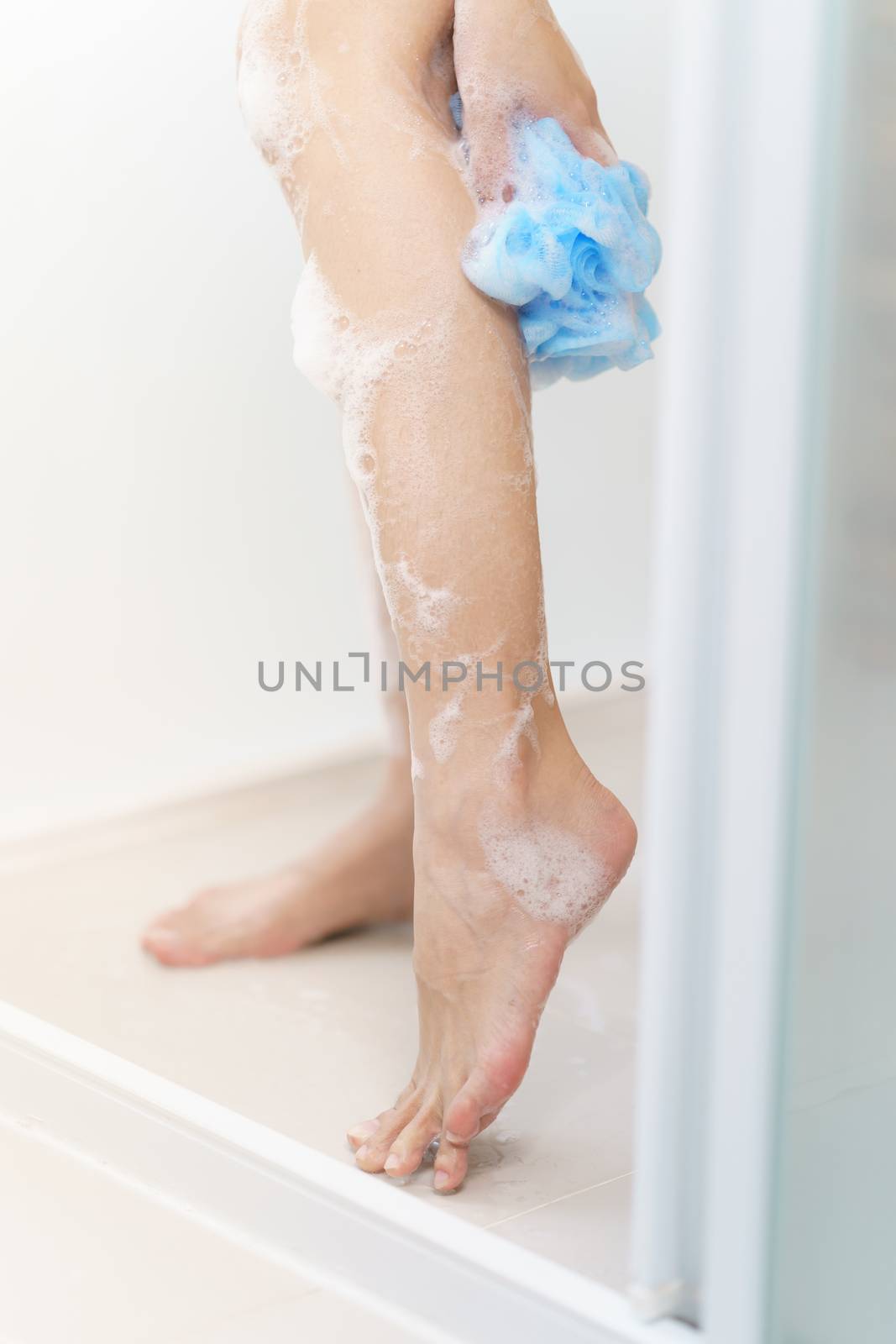 Woman washing her leg with bath sponge.