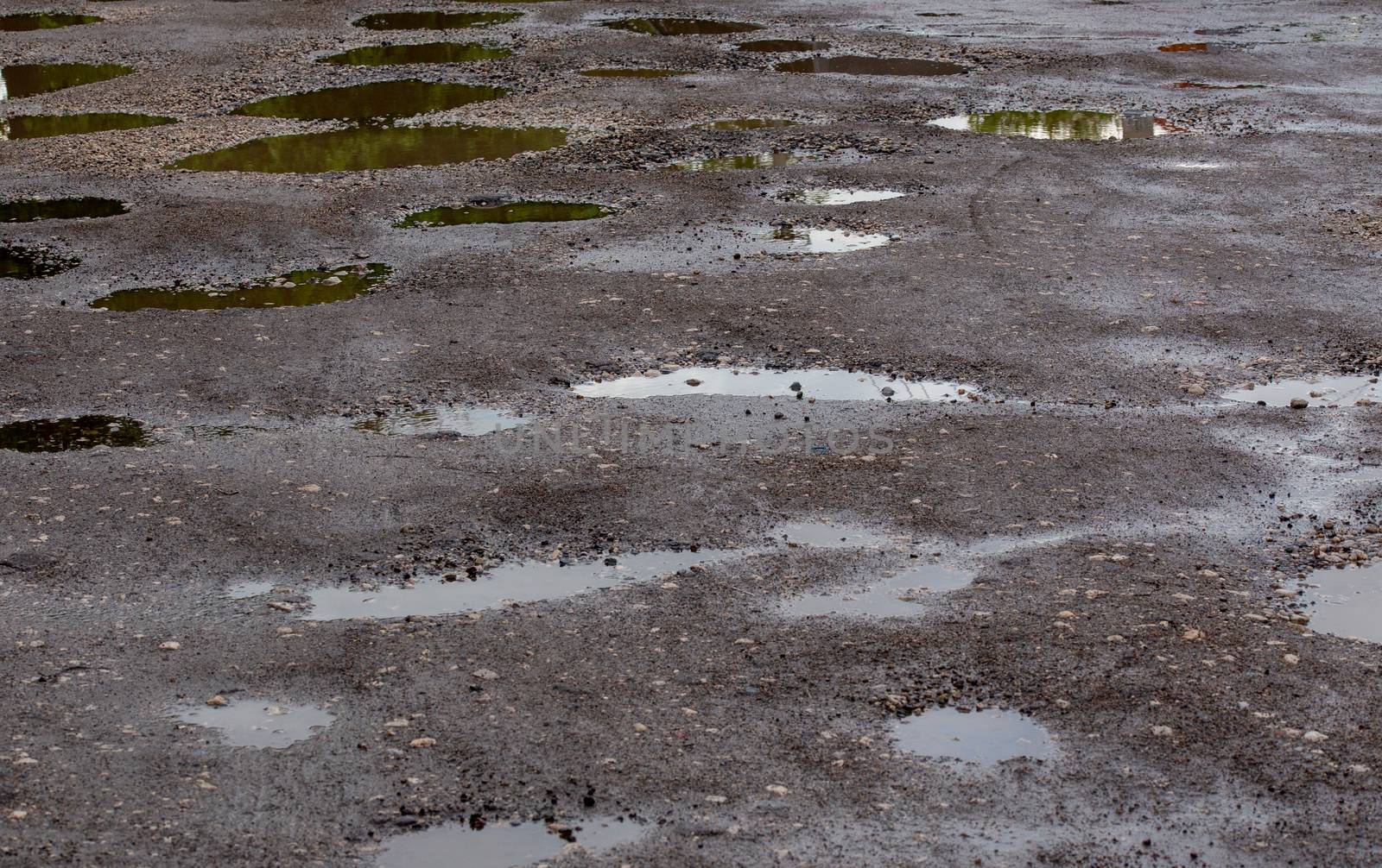 bumpy damaged road asphalt with multiple puddles after rain at summer daytime, potholes.